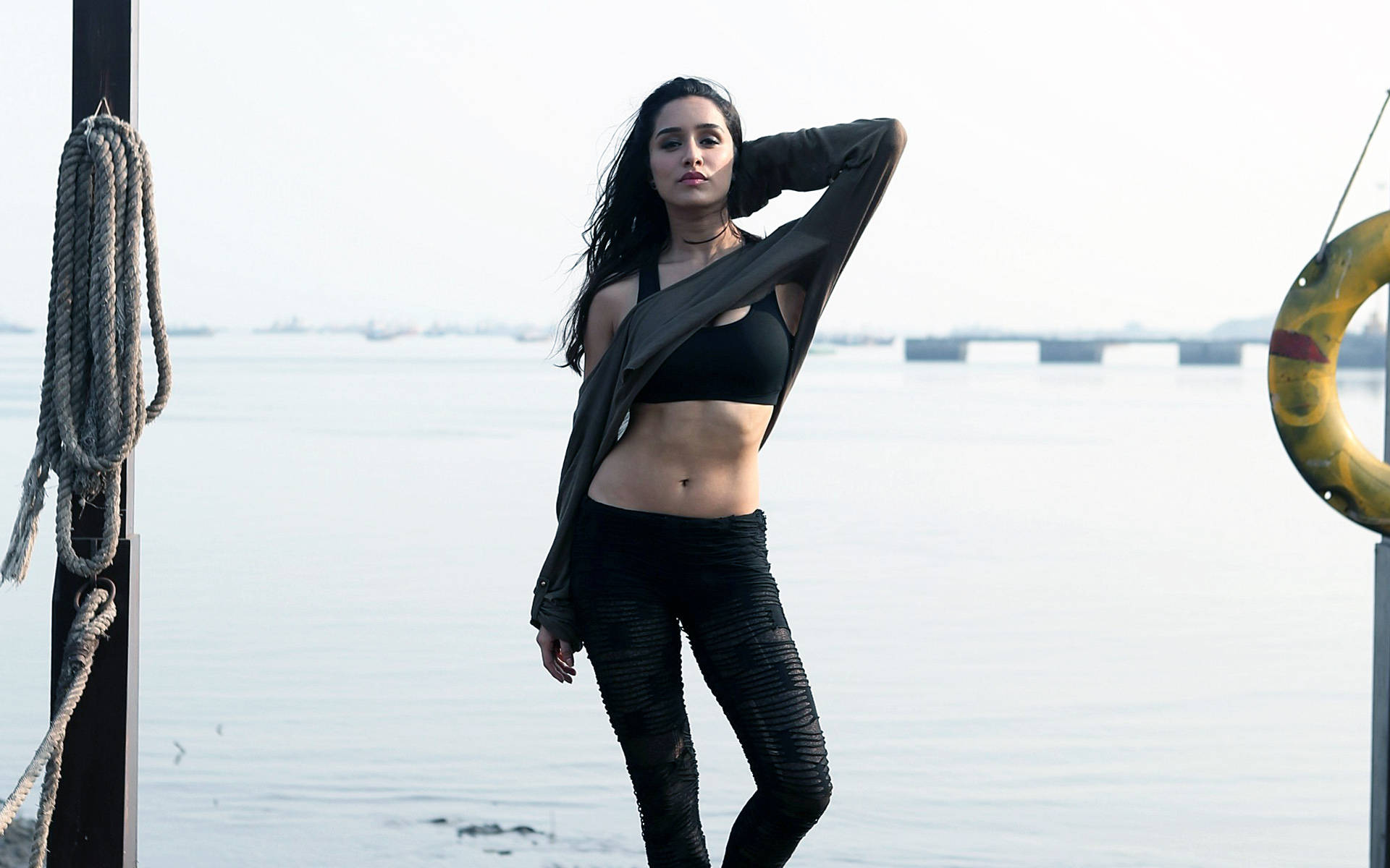 Shraddha Kapoor 桌布 壁紙 — 一名身穿黑色運動服的女性自信地在海濱碼頭旁擺姿勢，附近有救生圈和盤繞的繩索。