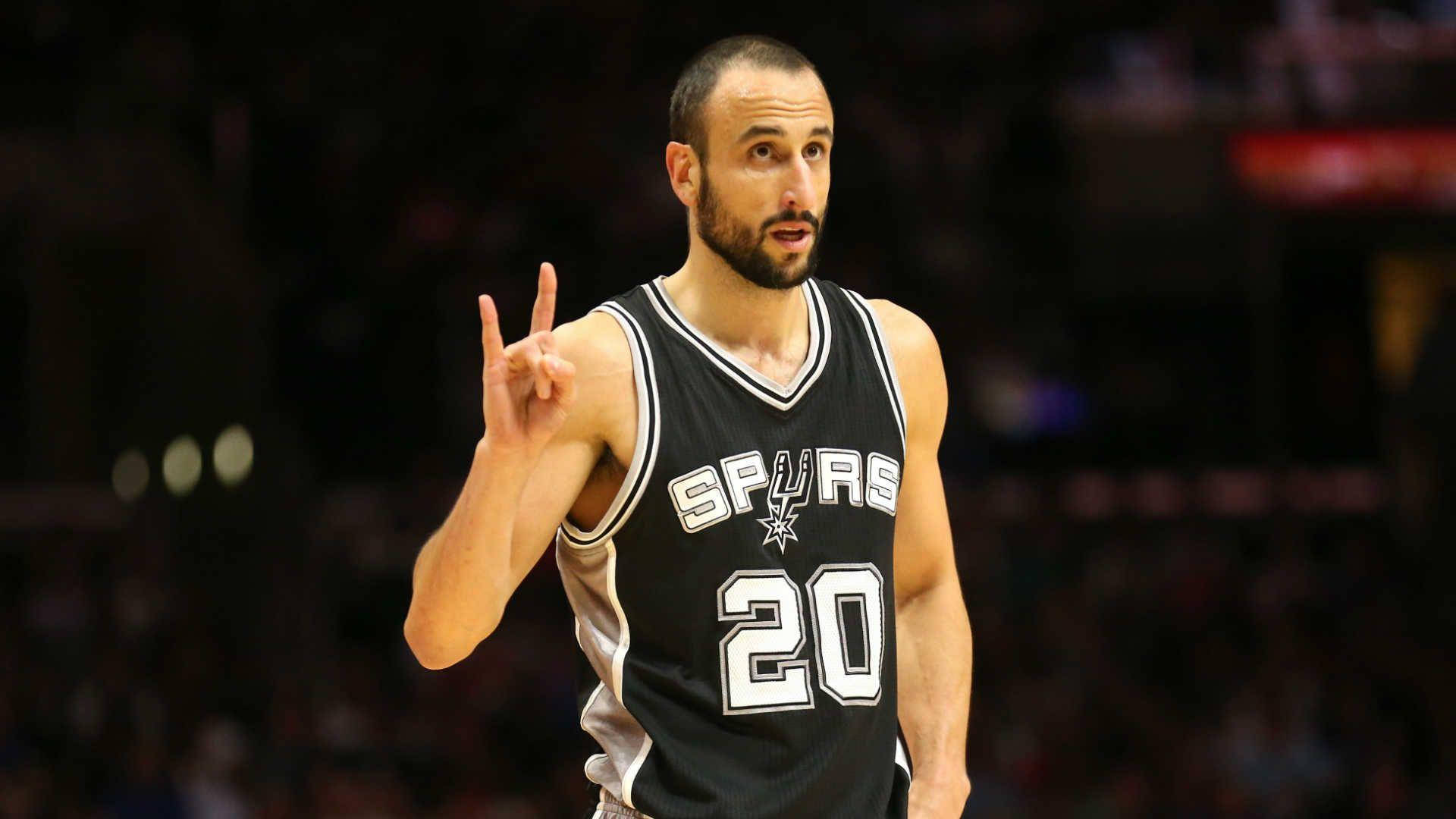 Manu 桌布 壁紙 — 一名身穿黑色馬刺球衣、背號20的籃球運動員在場館燈光下比賽時做出和平手勢。