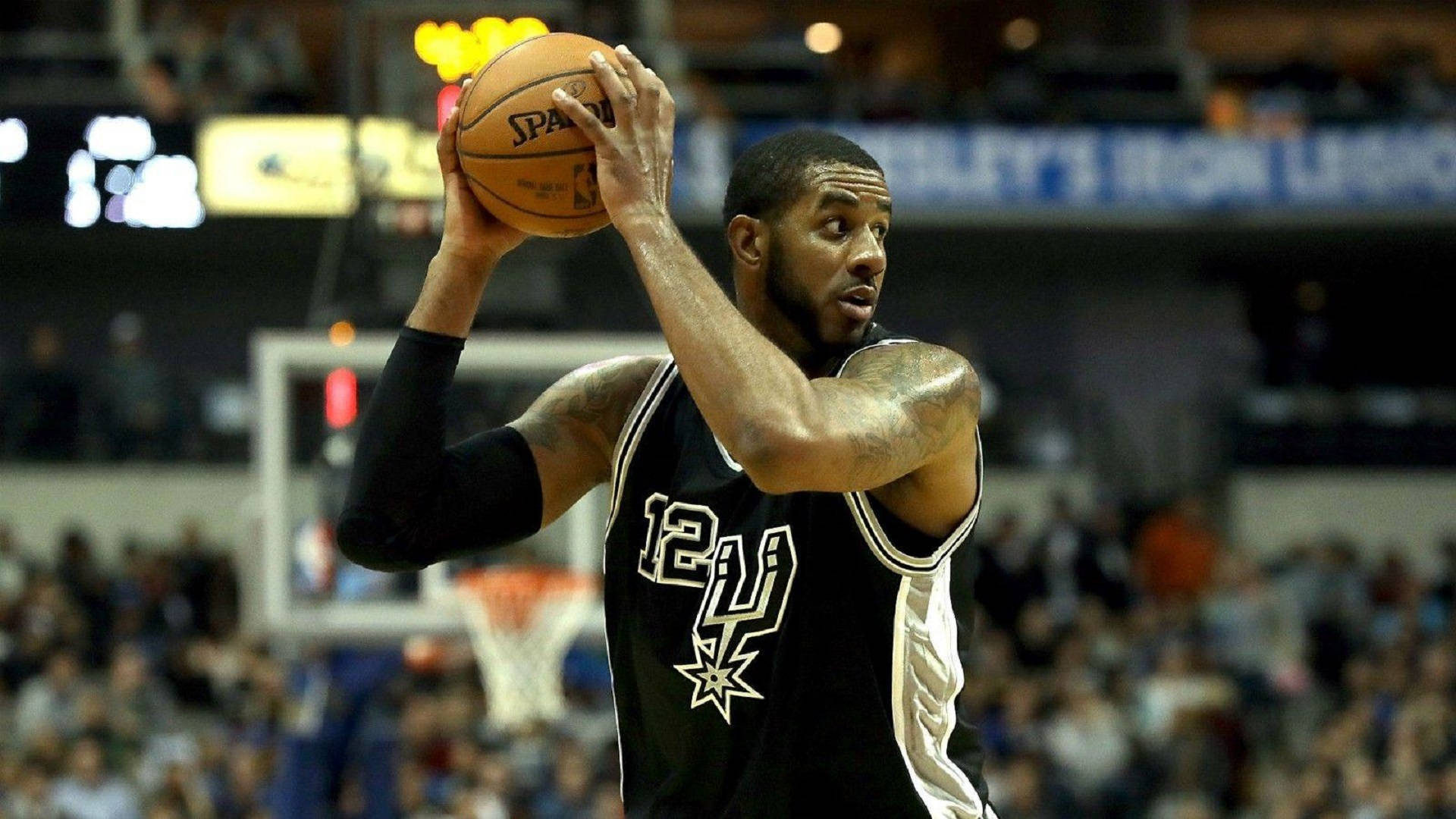 Lamarcus Aldridge 桌布 壁紙 — 一名身穿黑色馬刺隊球衣的籃球運動員在室內比賽中準備投籃，背景是模糊的人群。