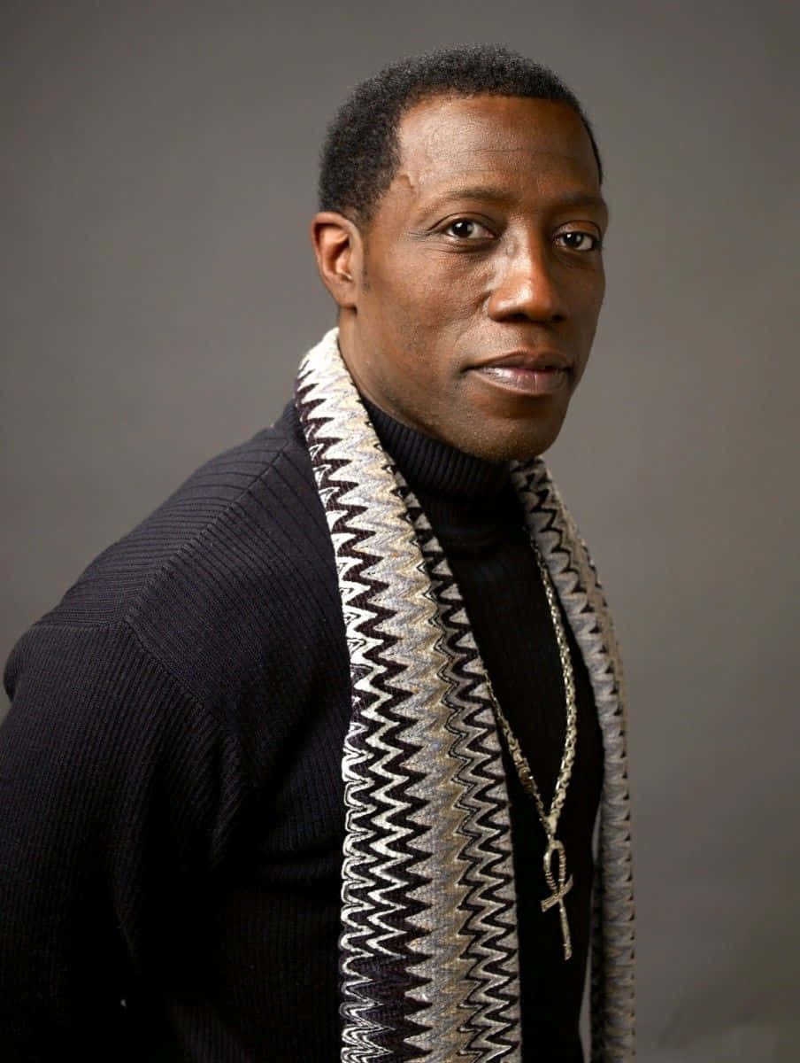 Wesley Snipes 桌布 壁紙 — 一名身穿黑色高領毛衣和圖案圍巾的男子，在灰色中性攝影棚背景前平靜地凝視。