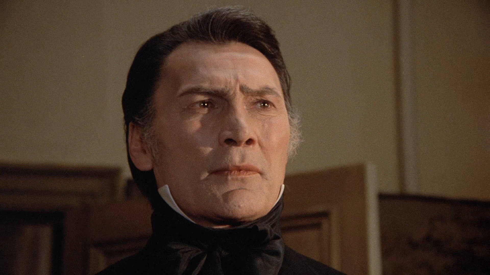 dracula 桌布 壁紙 — 一名身穿黑色高領襯衫的男子在溫暖的室內環境中向上凝視，表情嚴肅。