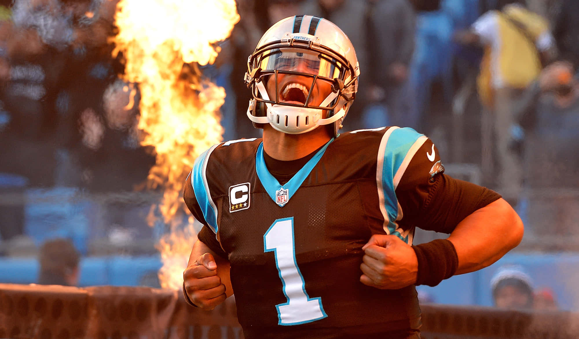 Cam Newton 桌布 壁紙 — 一名身穿黑藍色制服的美式足球四分衛緊握拳頭怒吼，身後球場上火焰噴發。