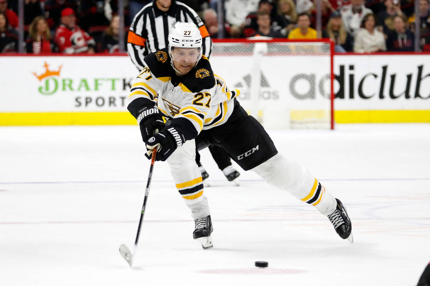 hockey 桌布 壁紙 — 一名身穿黑金色制服的冰球球員在比賽中向前傾，用球棍在冰上溜冰，背景有觀眾和裁判。