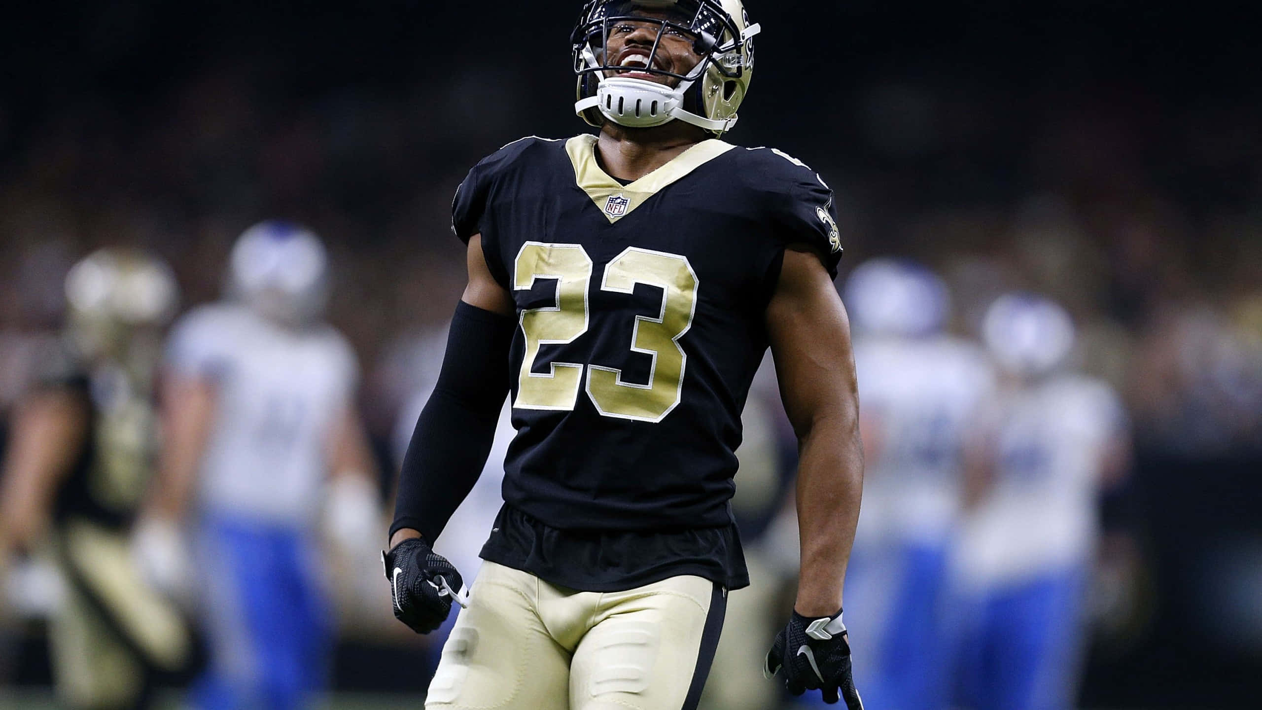 New Orleans Saints 桌布 壁紙 — 一名身穿黑金色球衣、號碼23的足球員在夜間比賽中於球場上燦爛微笑。
