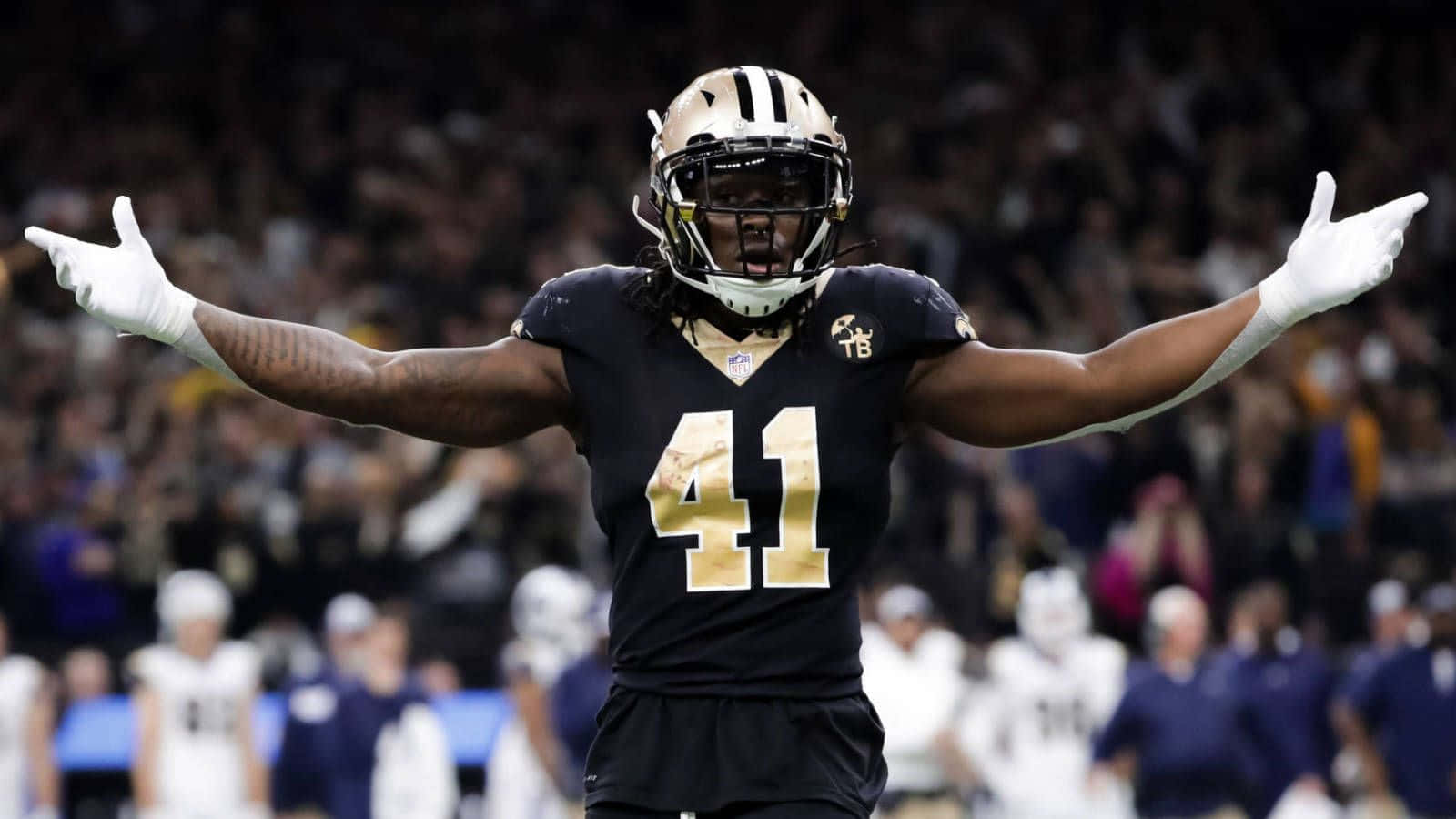 Alvin Kamara 桌布 壁紙 — 一名身穿黑金色球衣、號碼41的足球員在燈光球場上張開雙臂慶祝。