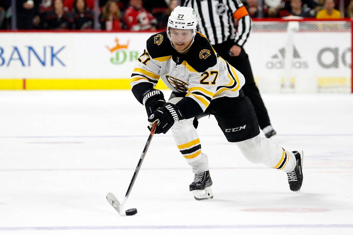 hockey 桌布 壁紙 — 一名身穿黑金色球衣的冰球運動員在明亮的場館燈光下，於激烈的比賽中帶著冰球向前滑行。