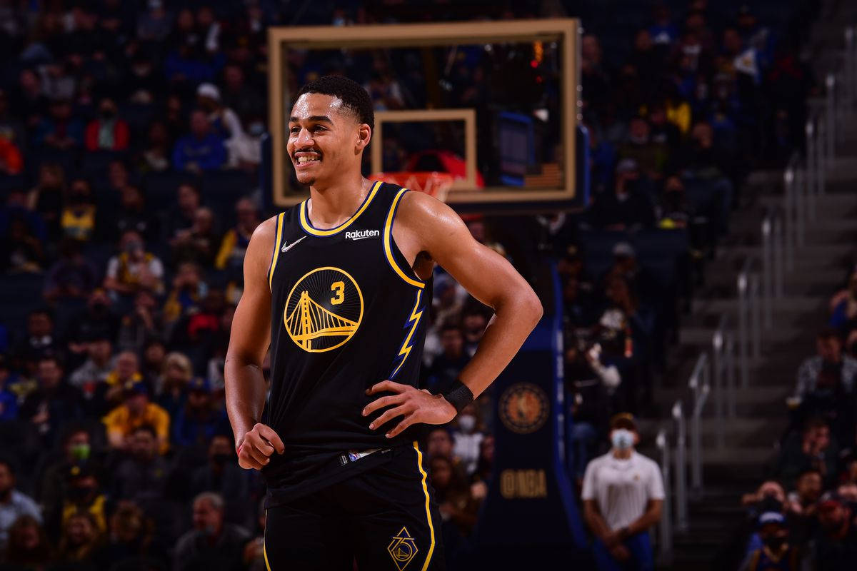 NBA 桌布 壁紙 — 一名身穿黑金色球衣的籃球運動員在燈光明亮的球場上自信地微笑，背景是人群。