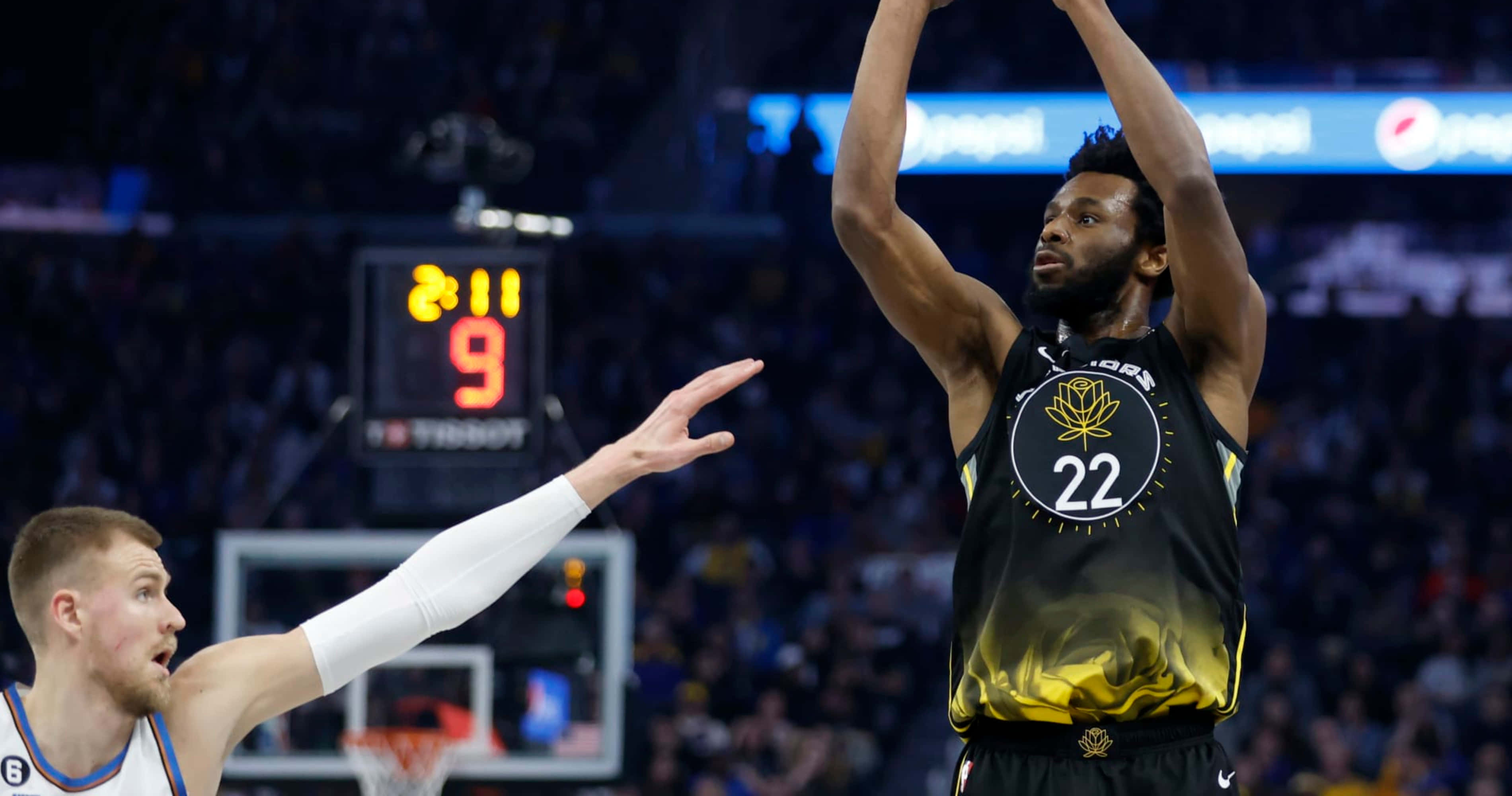 Andrew Wiggins 桌布 壁紙 — 一名身穿黑金色球衣的籃球運動員跳起投籃，而一名身穿白色袖套的防守球員伸展身體試圖封阻。