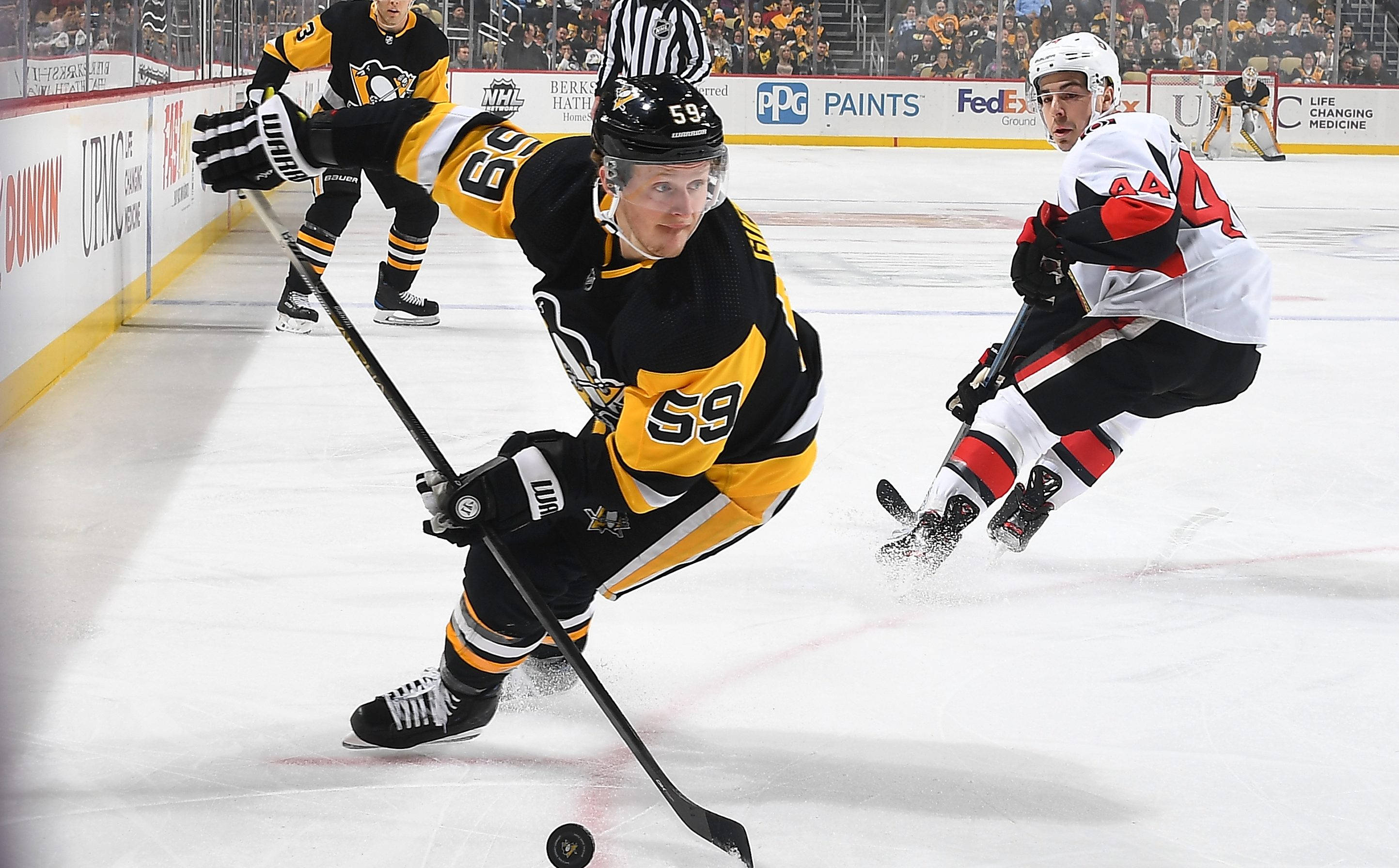 hockey 桌布 壁紙 — 一名身穿黑黃色球衣、號碼59的冰球運動員帶著冰球激烈滑行，而一名身穿白色球衣的對手在冰上追趕他。