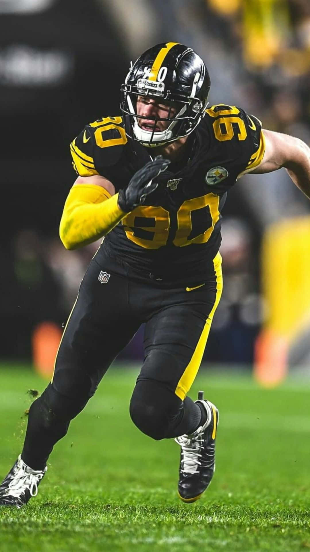 Steelers iPhone 桌布 壁紙 — 一名身穿黑黃色球衣的匹茲堡鋼人隊美式足球員在夜間比賽中於綠色球場上衝刺。