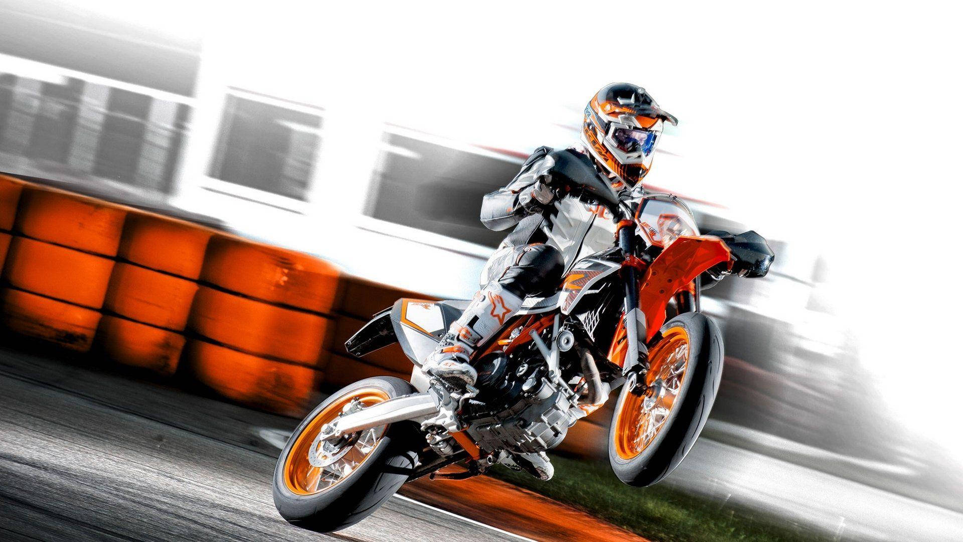 KTM 摩托車 桌布 壁紙 — 一名車手在賽道上騎著橙白色越野摩托車傾斜入彎，背景有模糊的動感和鮮豔的橙色護欄。