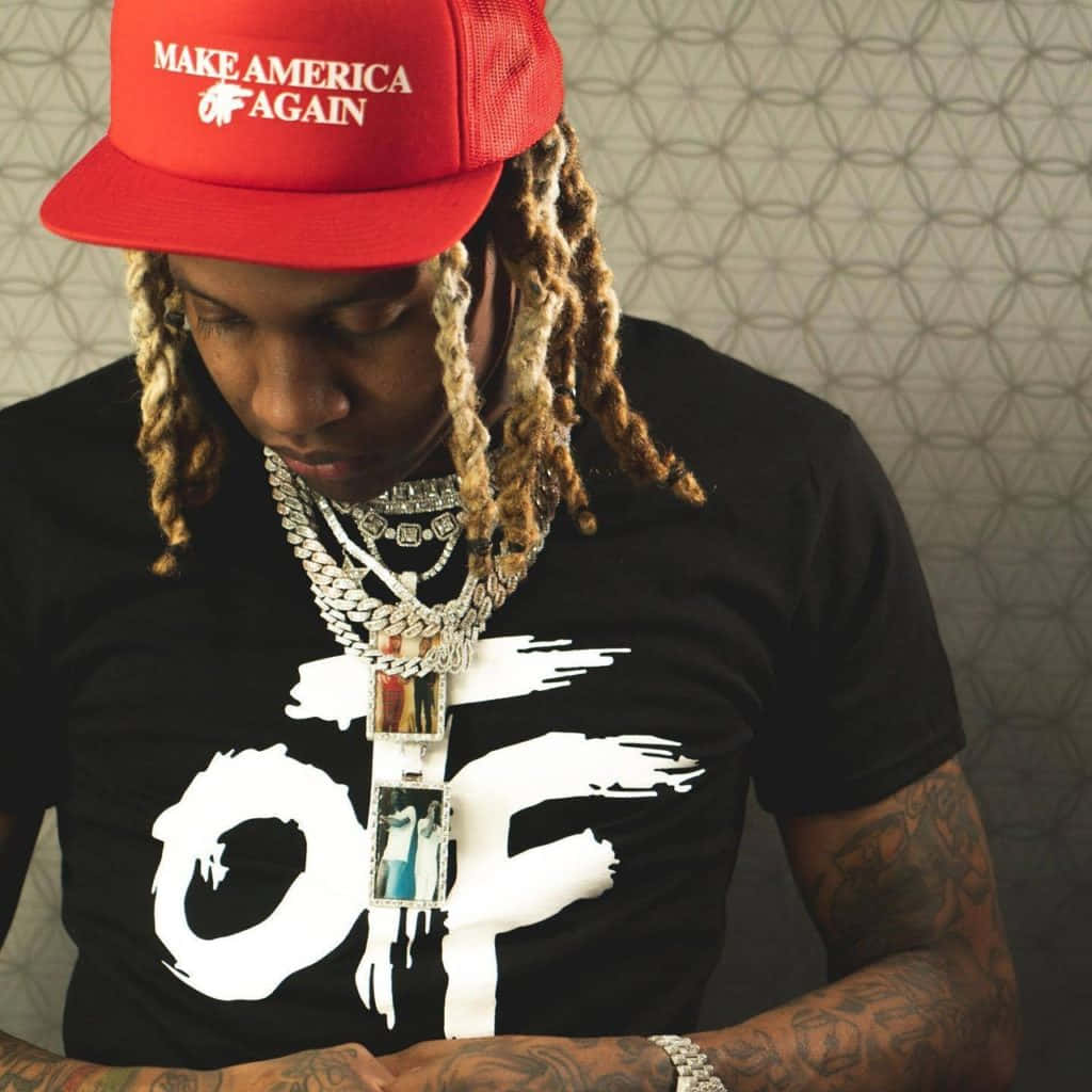Lil Durk 桌布 壁紙 — 一名辮子男戴著紅色「Make America Again」帽子和多層銀鏈，背景是有圖案的牆壁。
