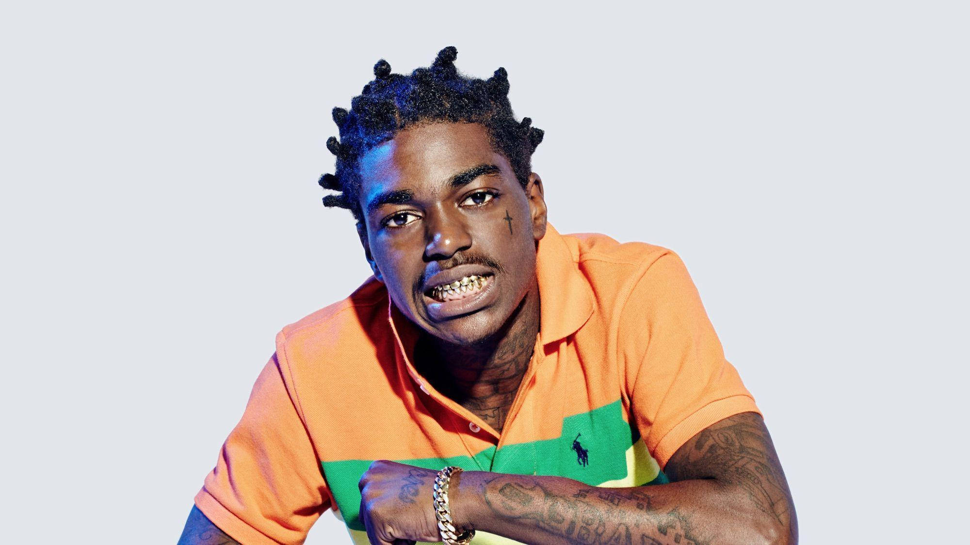 Kodak 桌布 壁紙 — 一名辮子頭髮和刺青的男子，穿著橙色Polo衫，背景是純淺灰色。
