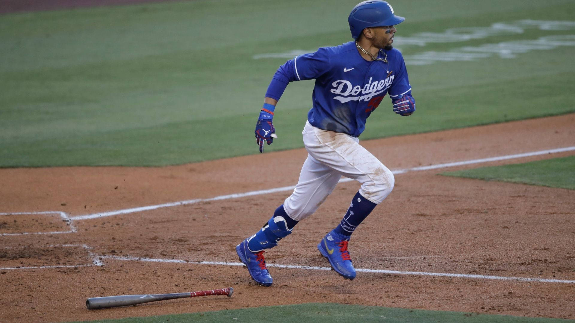 Mookie Betts 桌布 壁紙 — 一名道奇隊棒球選手在比賽期間衝過本壘板，他的球棒躺在泥土內野上。