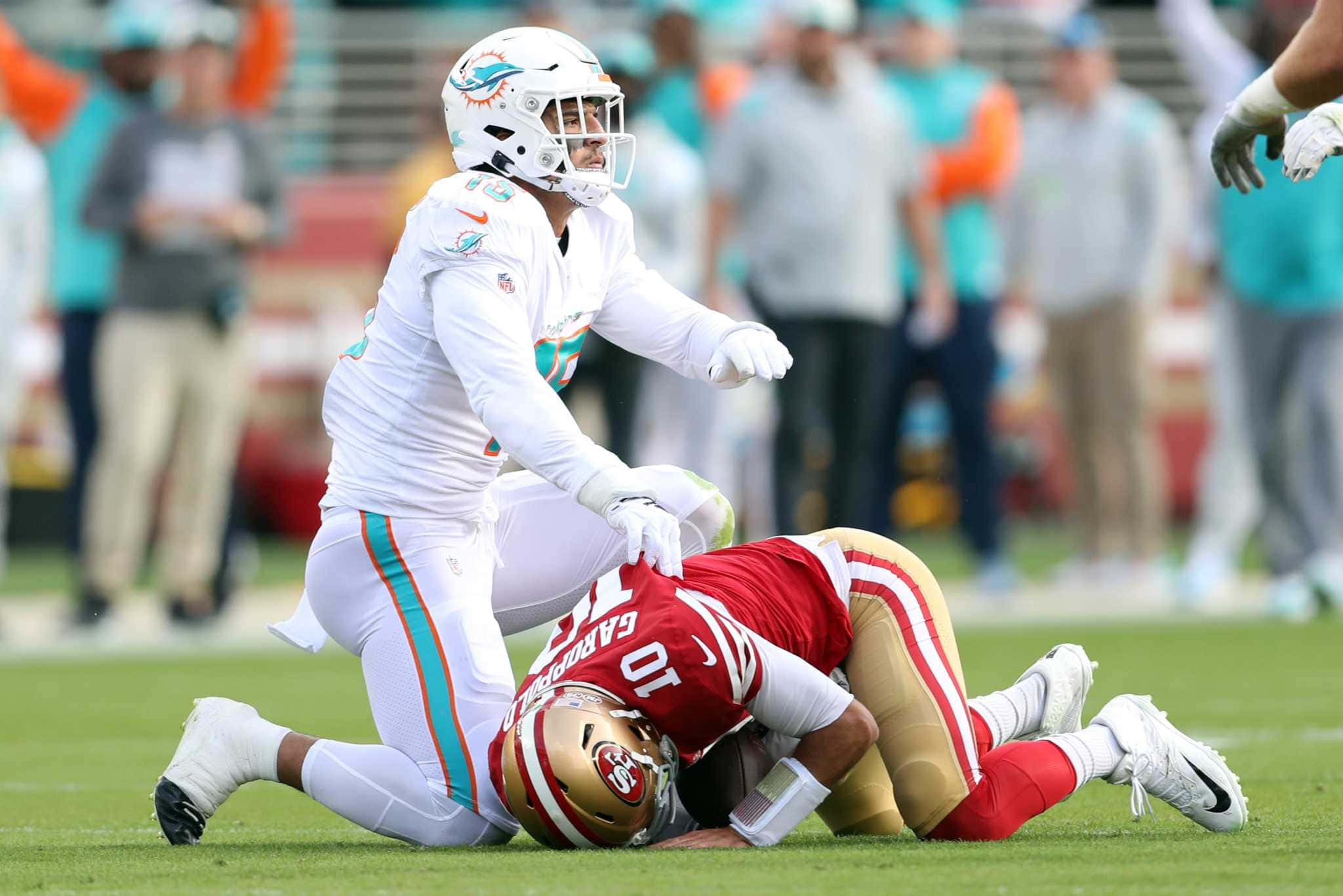 Jimmy Garoppolo 桌布 壁紙 — 一名邁阿密海豚隊球員在陽光明媚的足球場上跪在倒下的舊金山49人隊球員身上。