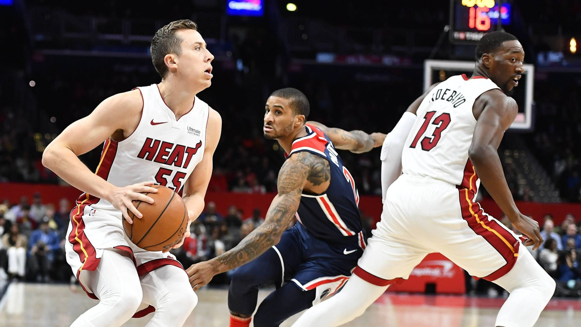 duncan robinson 桌布 壁紙 — 一名邁阿密熱火球員在場館燈光下進行高能量籃球比賽時，運球並被兩名對手緊密防守。
