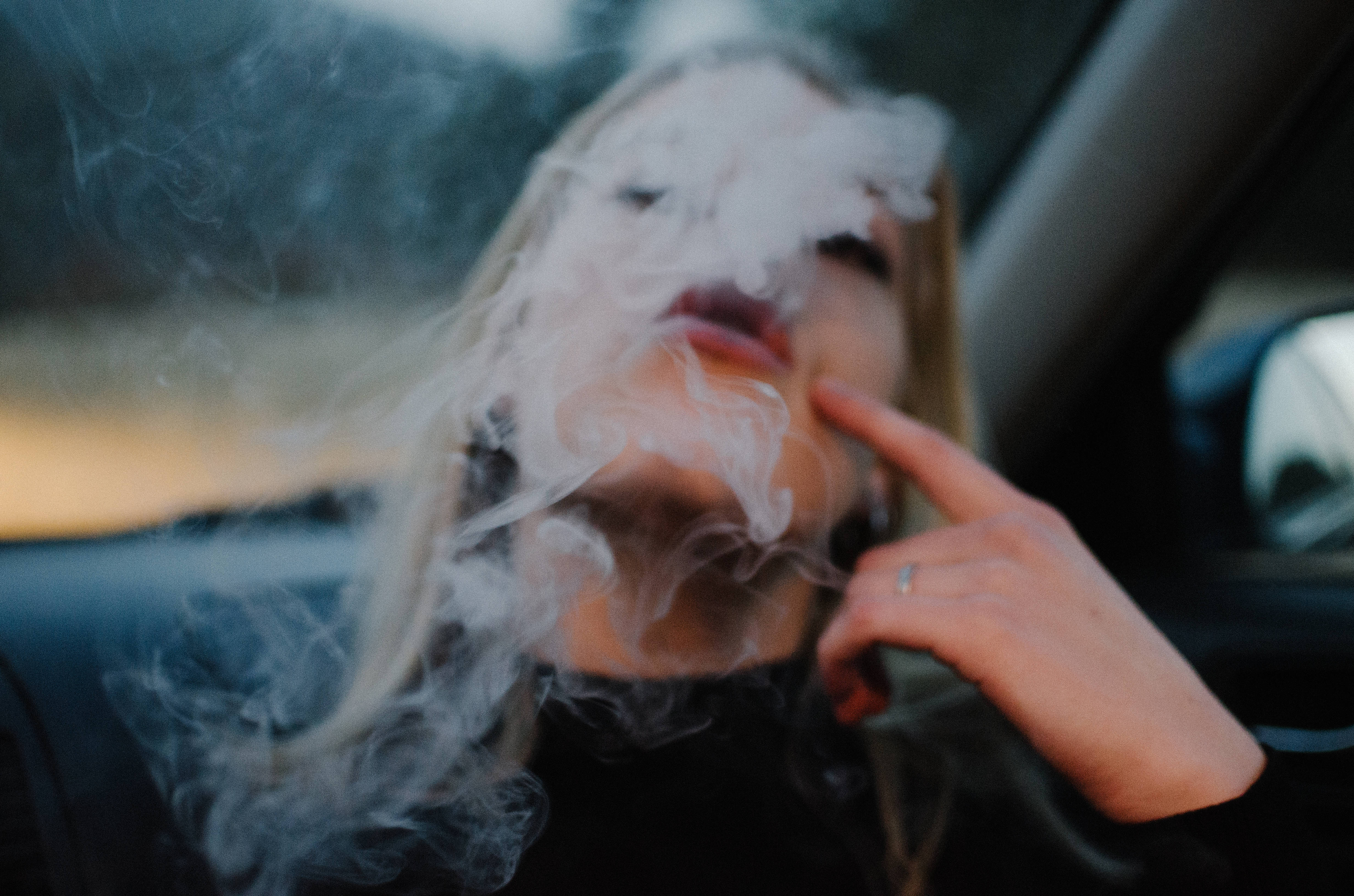 吸大麻 桌布 壁紙 — 一名金髮人士在車內呼出濃煙，同時指著自己的嘴唇。