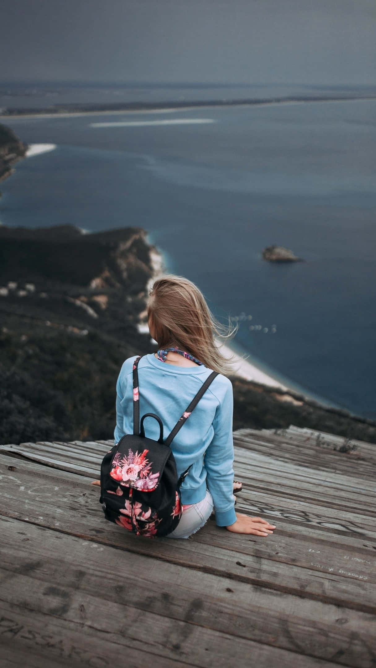Beach Bag 桌布 壁紙 — 一名金髮人士坐在飽經風霜的木甲板上，俯瞰陰沉灰天下廣闊的海洋。