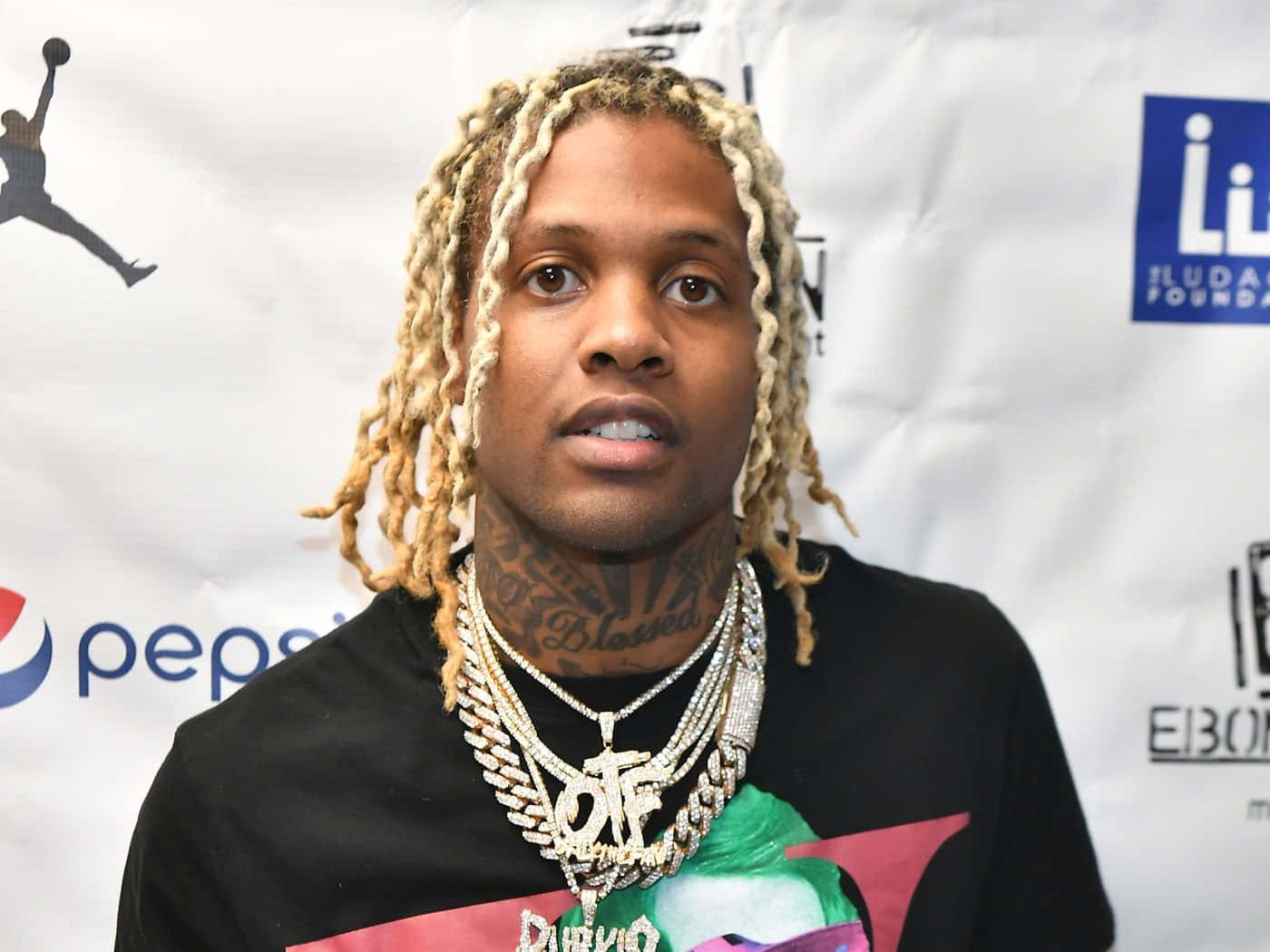 Lil Durk 桌布 壁紙 — 一名金髮辮子、戴著厚重金鏈的男子在印有百事可樂和喬丹標誌的品牌活動背景前擺姿勢。