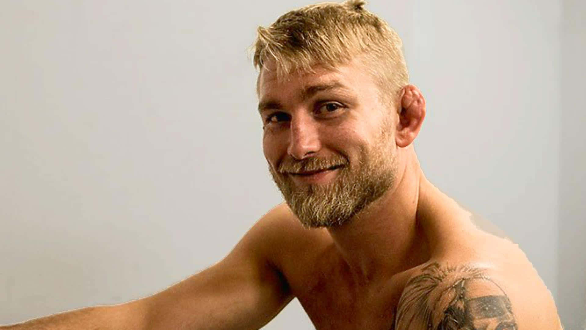 UFC 桌布 壁紙 — 一名金髮鬍鬚的赤裸上身男子，在純淺灰色背景前溫暖微笑。