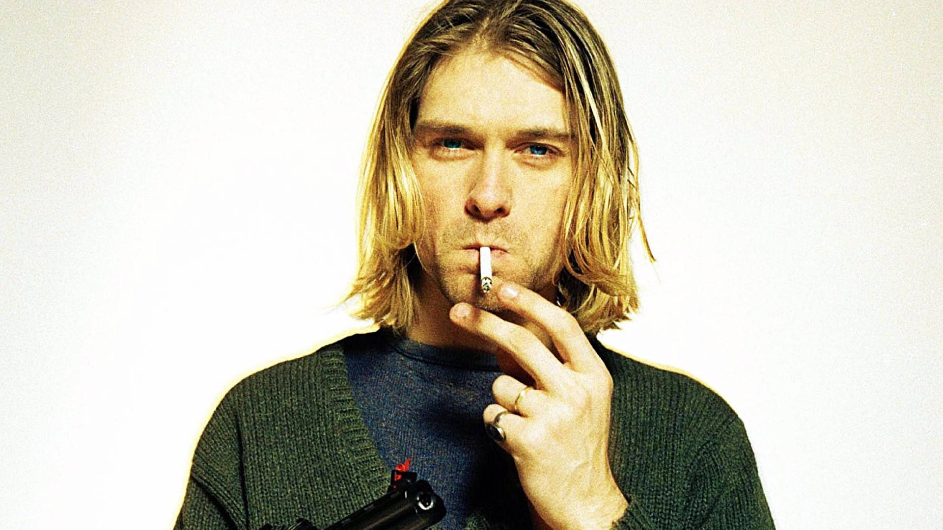 Cobain 桌布 壁紙 — 一名長金髮的男子在純白背景前抽煙，身穿綠色毛衣。
