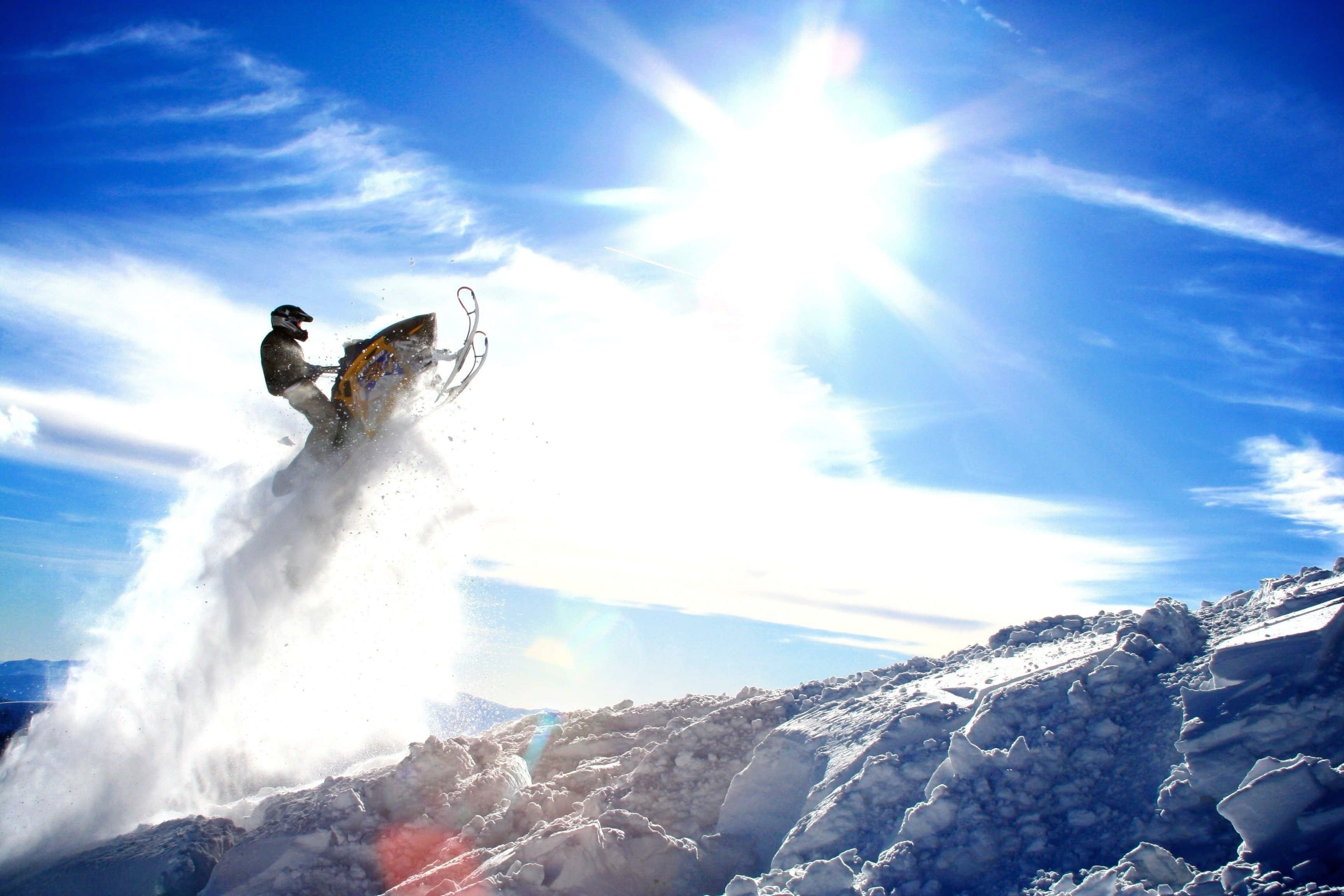 Winter Sports 桌布 壁紙 — 一名雪地摩托車手在熾熱的陽光下，飛越白雪覆蓋的山脊。