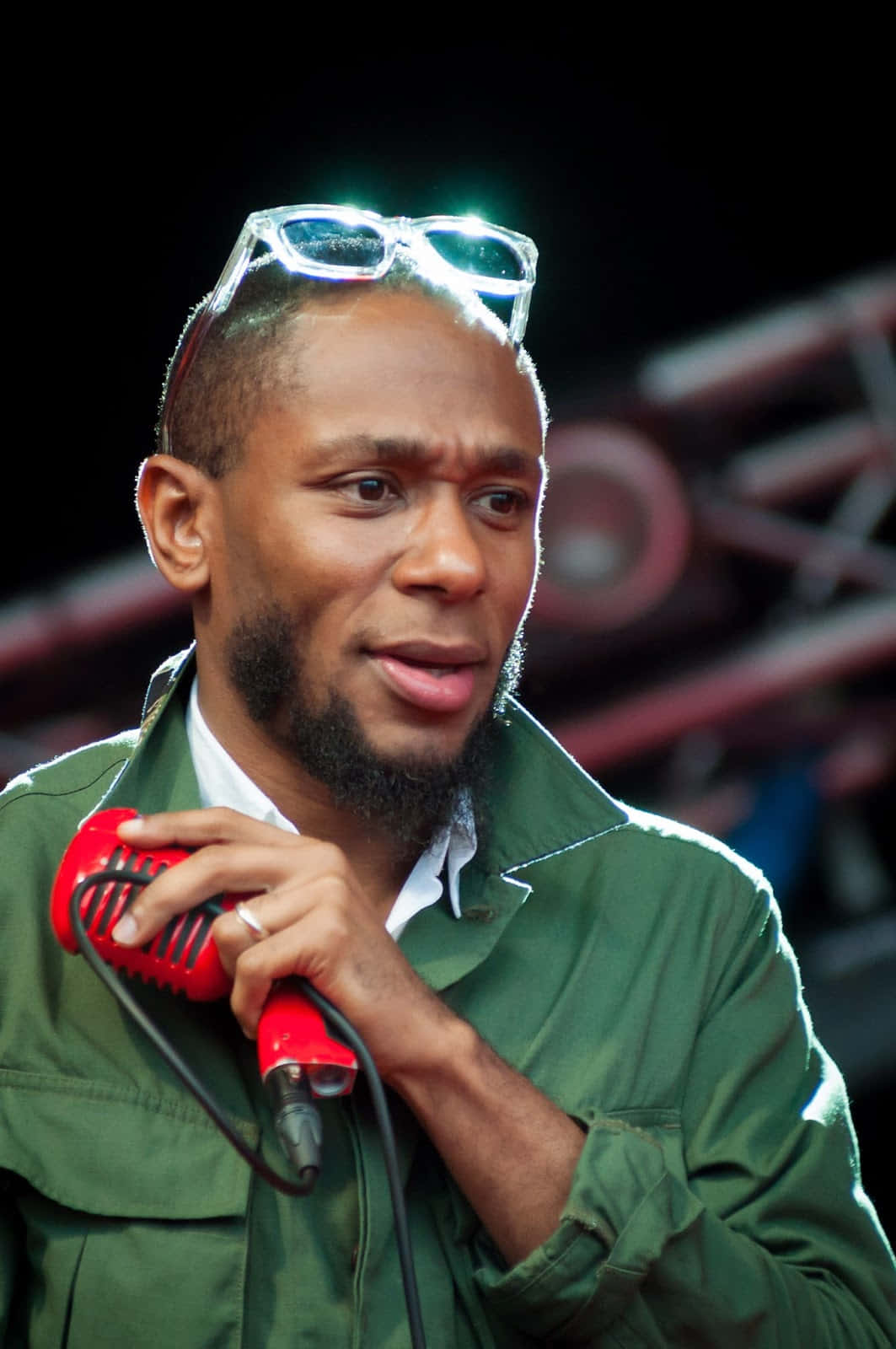 Yasiin Bey 桌布 壁紙 — 一名頭戴眼鏡的男子在明亮的舞台燈光下拿著紅色麥克風表演。