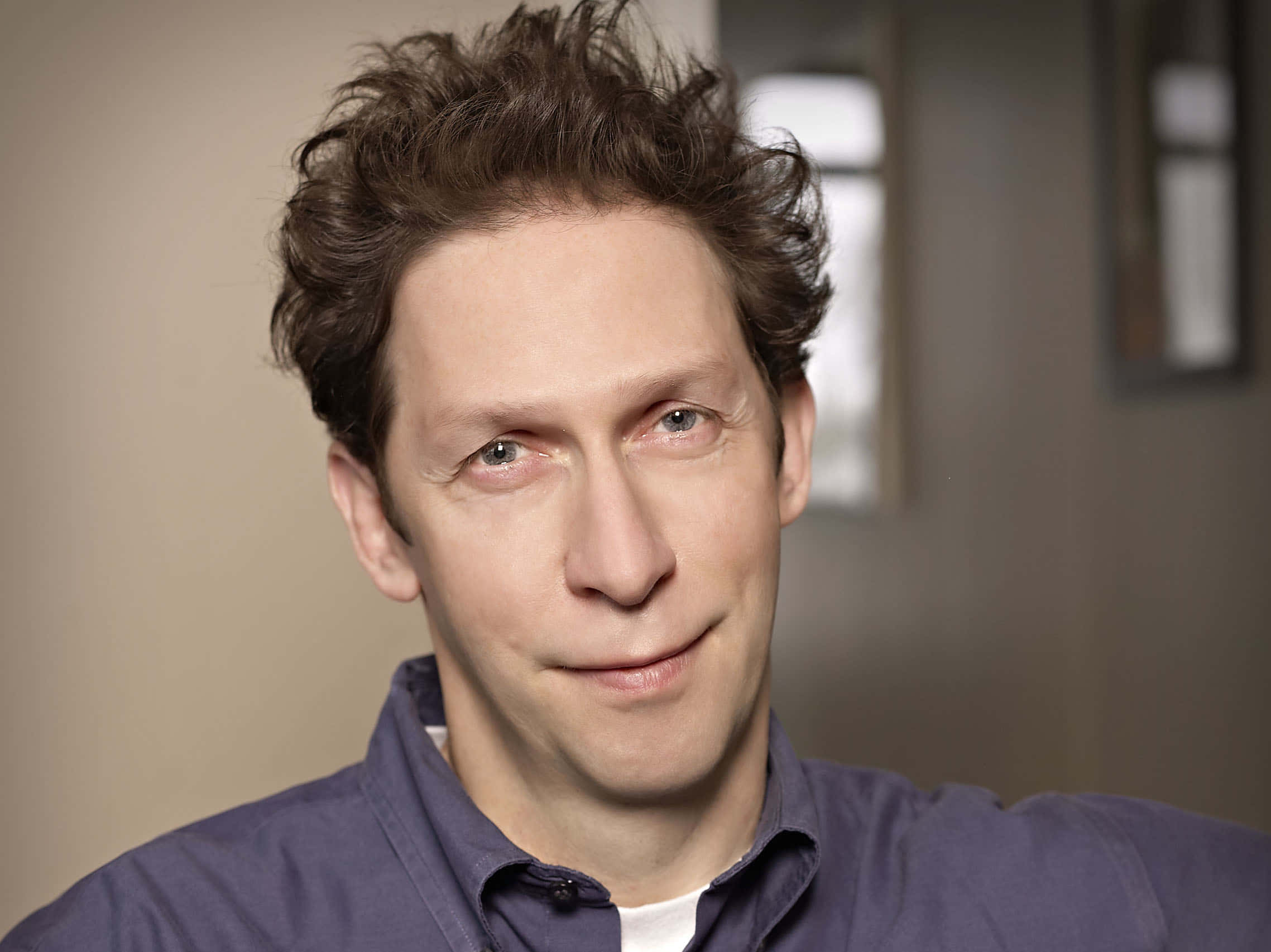 Tim Blake Nelson 桌布 壁紙 — 一名頭髮凌亂的棕色頭髮、帶著微妙微笑、身穿藍色襯衫的男士特寫肖像。
