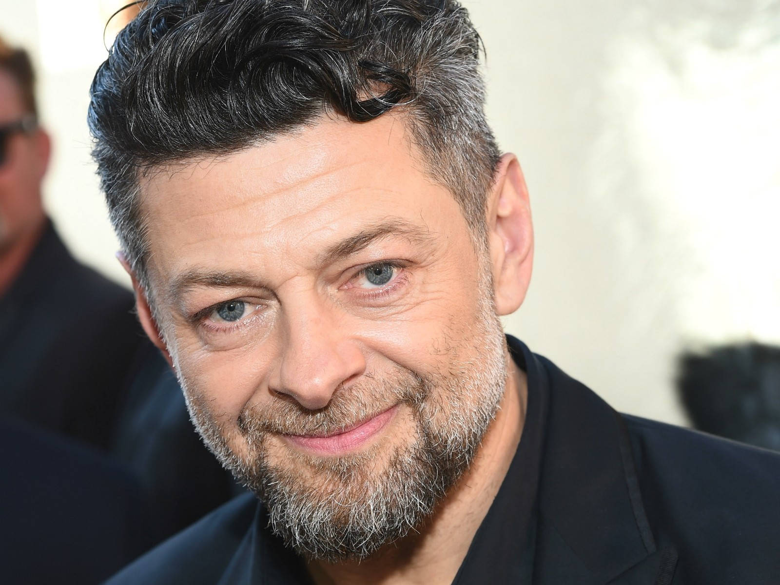 actor 桌布 壁紙 — 一名頭髮花白、留著鬍鬚的男子穿著深色西裝，溫暖微笑的特寫肖像。