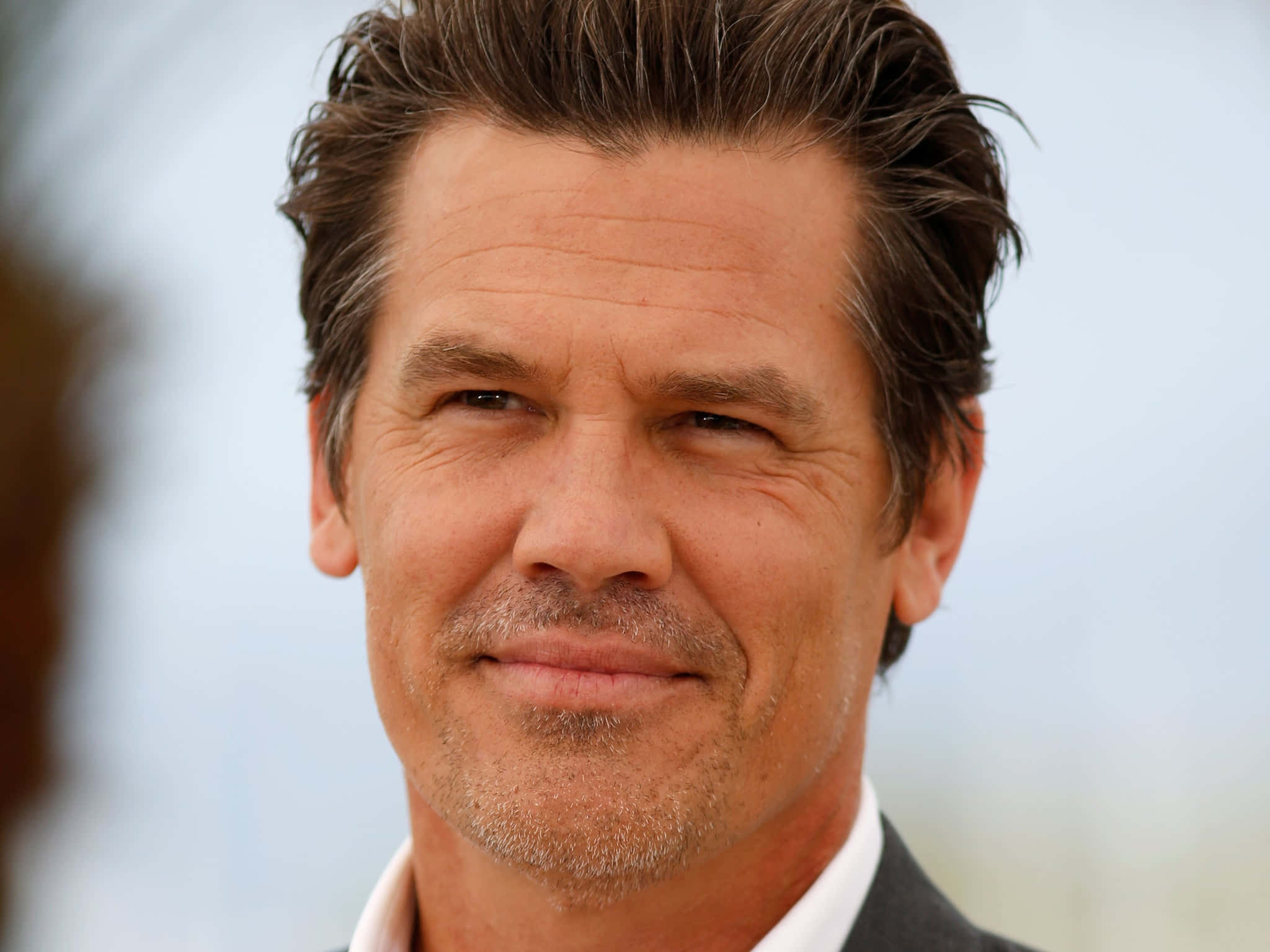 Josh Brolin 桌布 壁紙 — 一名頭髮花白、鬍渣未刮的男子在模糊背景前微笑的特寫肖像。