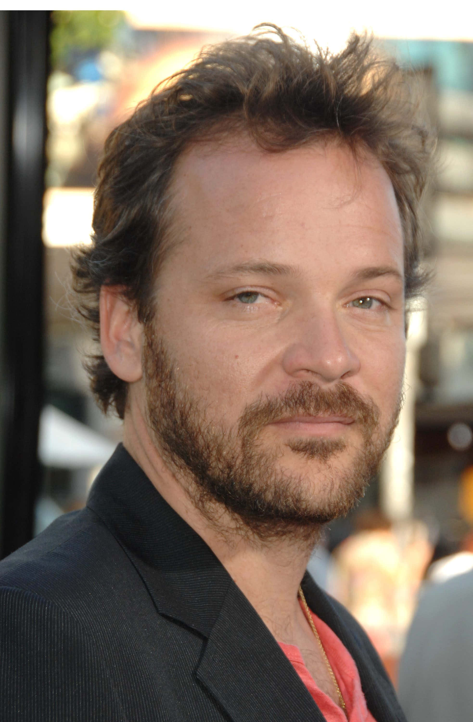 Peter Sarsgaard 桌布 壁紙 — 一名頭髮蓬鬆棕色、留鬍鬚的男士特寫肖像，身穿深色西裝外套內搭珊瑚色襯衫。