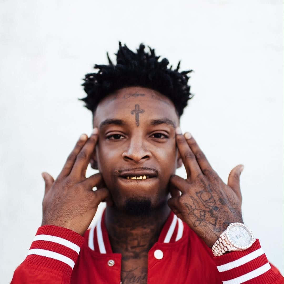 21 Savage 桌布 壁紙 — 一名額頭有十字刺青、雙手佈滿刺青的男子，在純白背景前將手指按在太陽穴上。