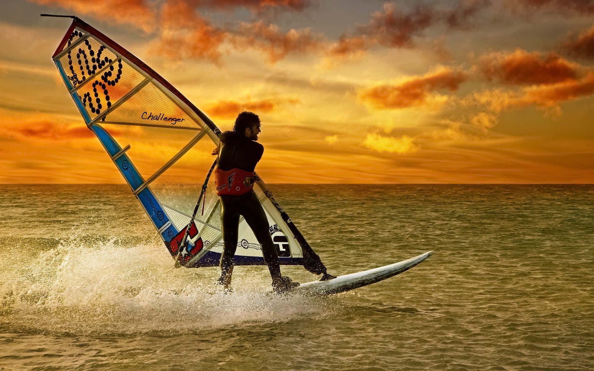 Beach Water Sports 桌布 壁紙 — 一名風帆滑浪者在日落時分滑過金色水面，背後是充滿活力的橙色天空和戲劇性的雲層。