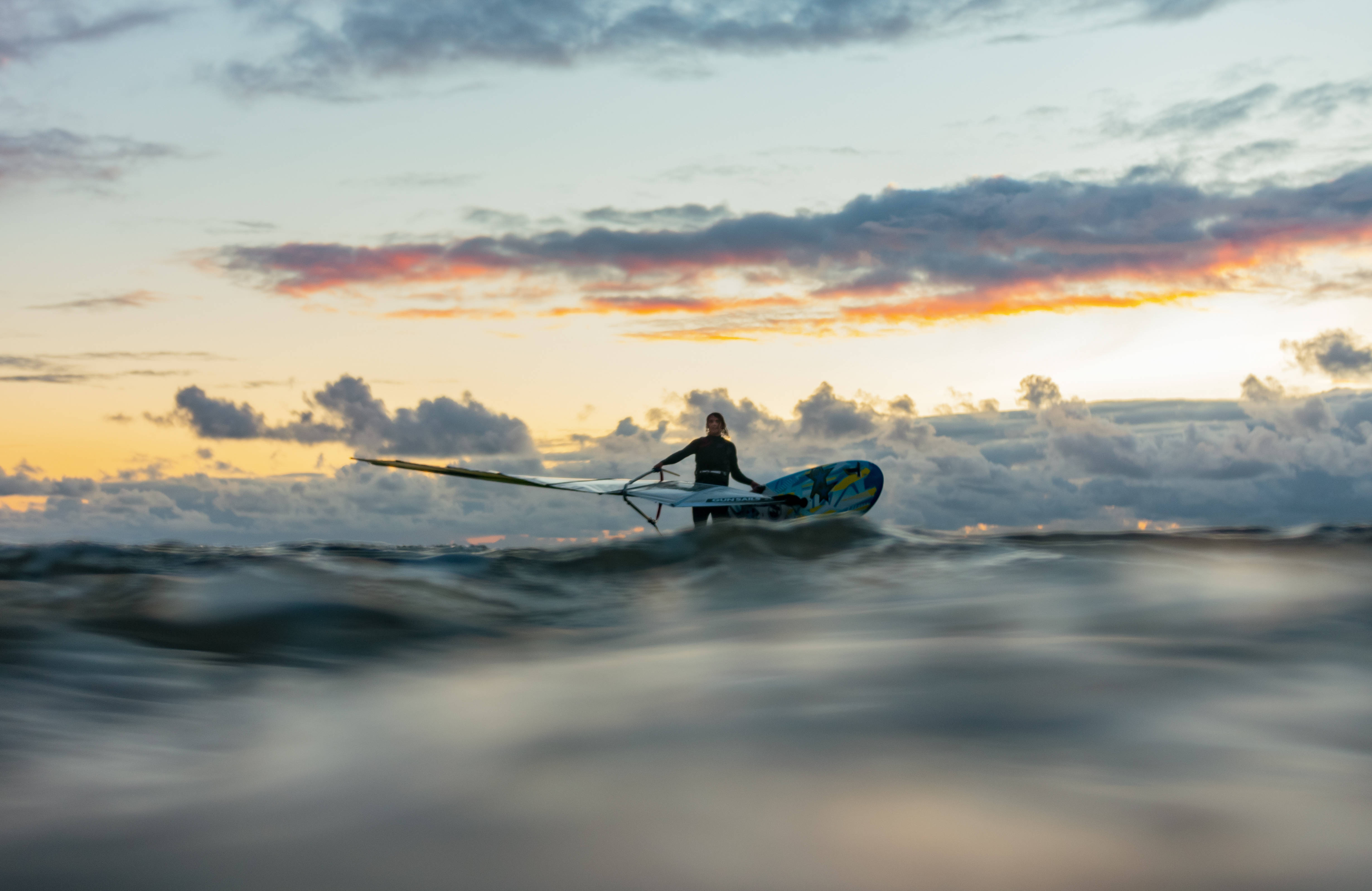 Windsurfing 桌布 壁紙 — 一名風帆衝浪者在日落時分掠過波濤洶湧的水面，上方是火紅的橙色和粉紅色雲彩。
