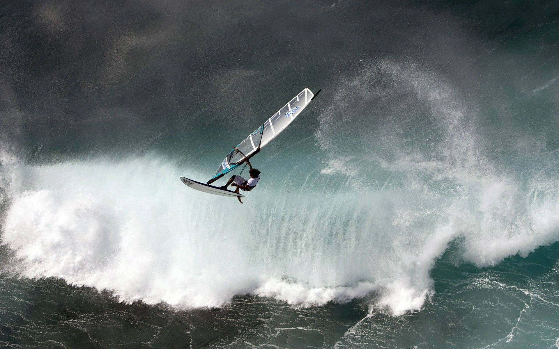 Windsurfing 桌布 壁紙 — 一名風帆衝浪者在暴風雨的天空下，在海浪破碎的浪花之上騰空飛翔。