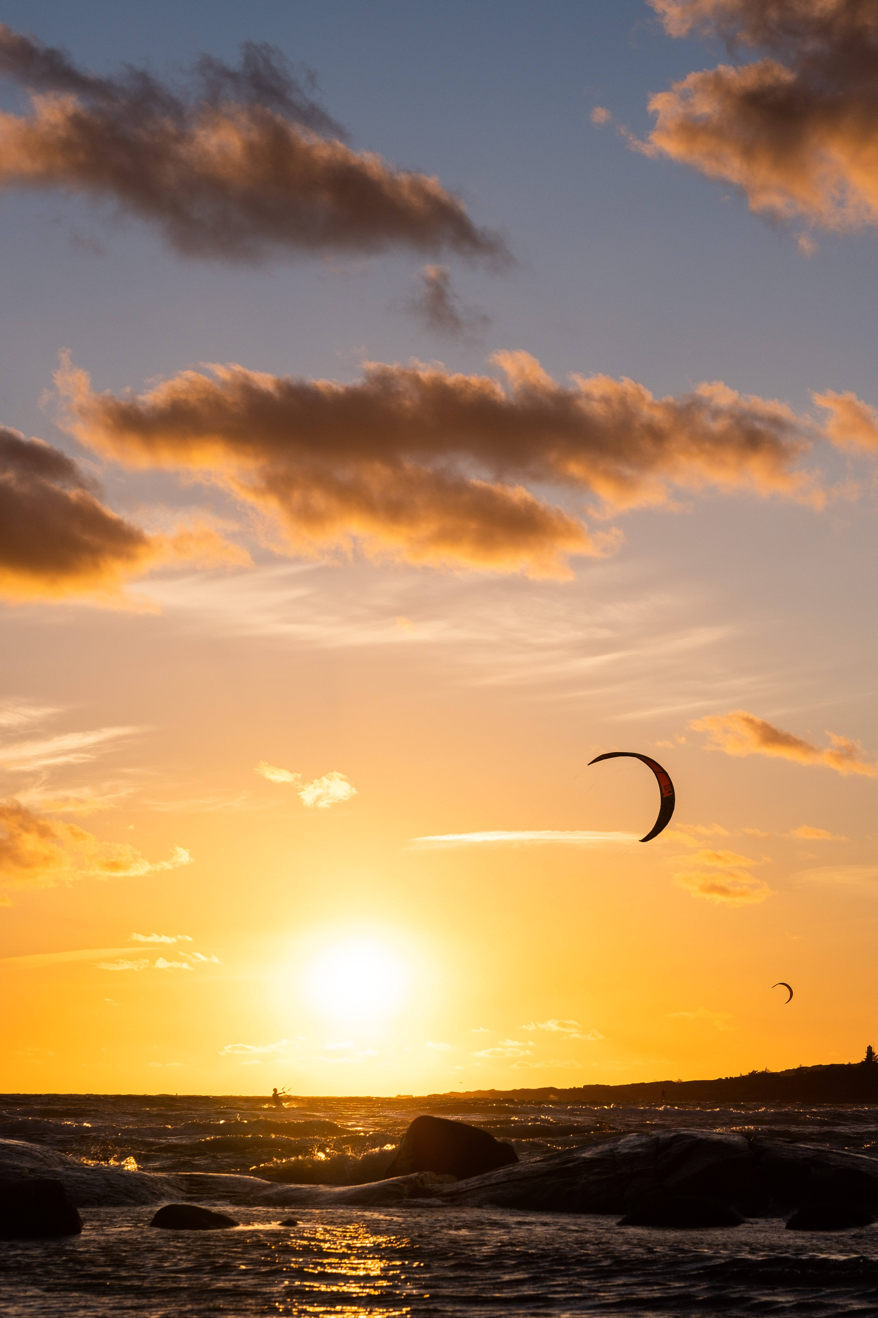 Paragliding 桌布 壁紙 — 一名風箏衝浪者在日落時分滑過金色水域，雲朵在藍天下發出橙色光芒。