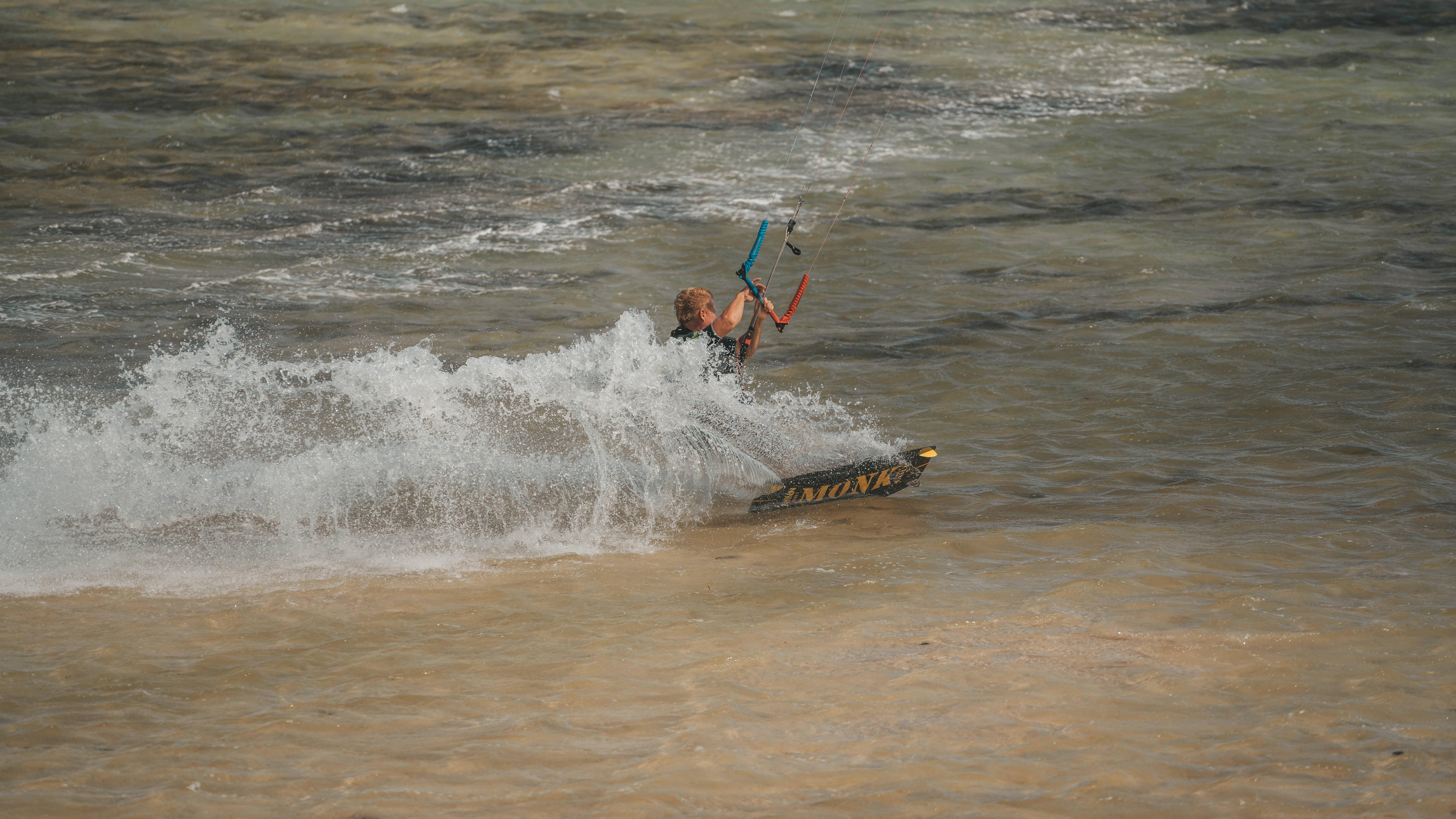 Windsurfing 桌布 壁紙 — 一名風箏衝浪者騎著帶有品牌標誌的板衝浪，穿過渾濁的水面，水花四濺。
