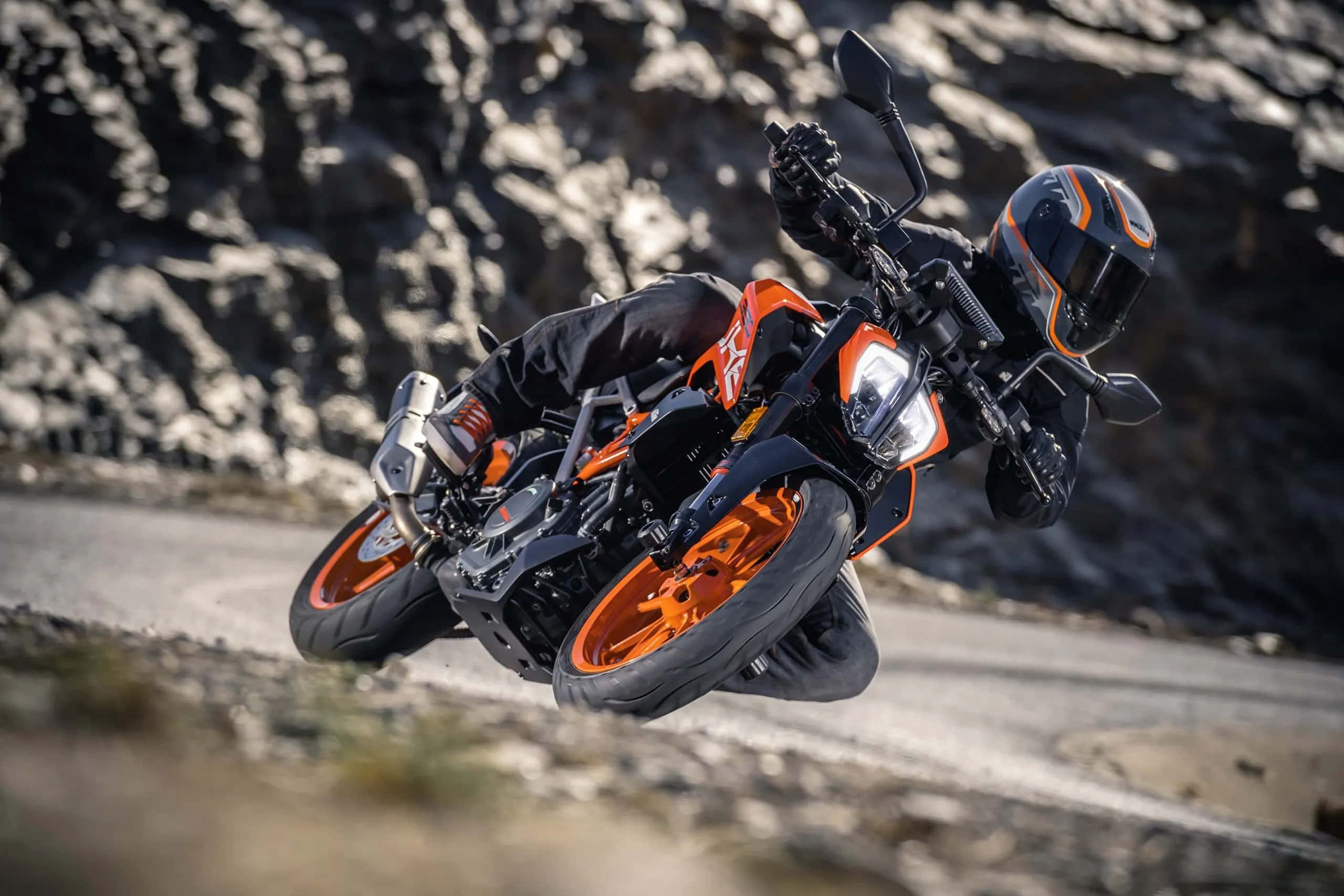 機車 桌布 壁紙 — 一名騎士在岩石山路上方凌空騎著橙色KTM機車傾身進入急彎。