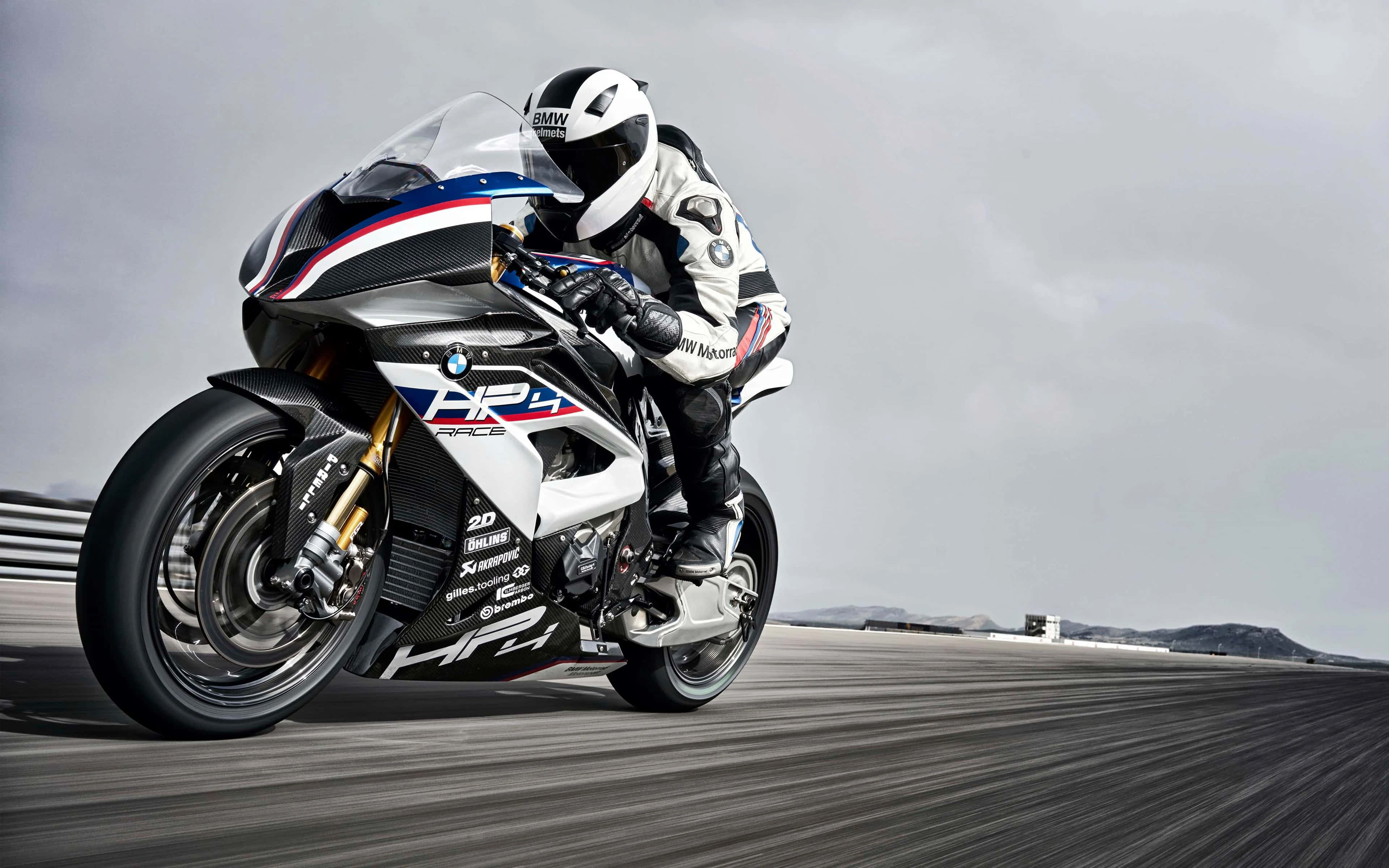 motorbike 桌布 壁紙 — 一名騎士在灰色賽道上，騎著白色、藍色和紅色的BMW HP4 Race摩托車，在陰天傾身入彎。