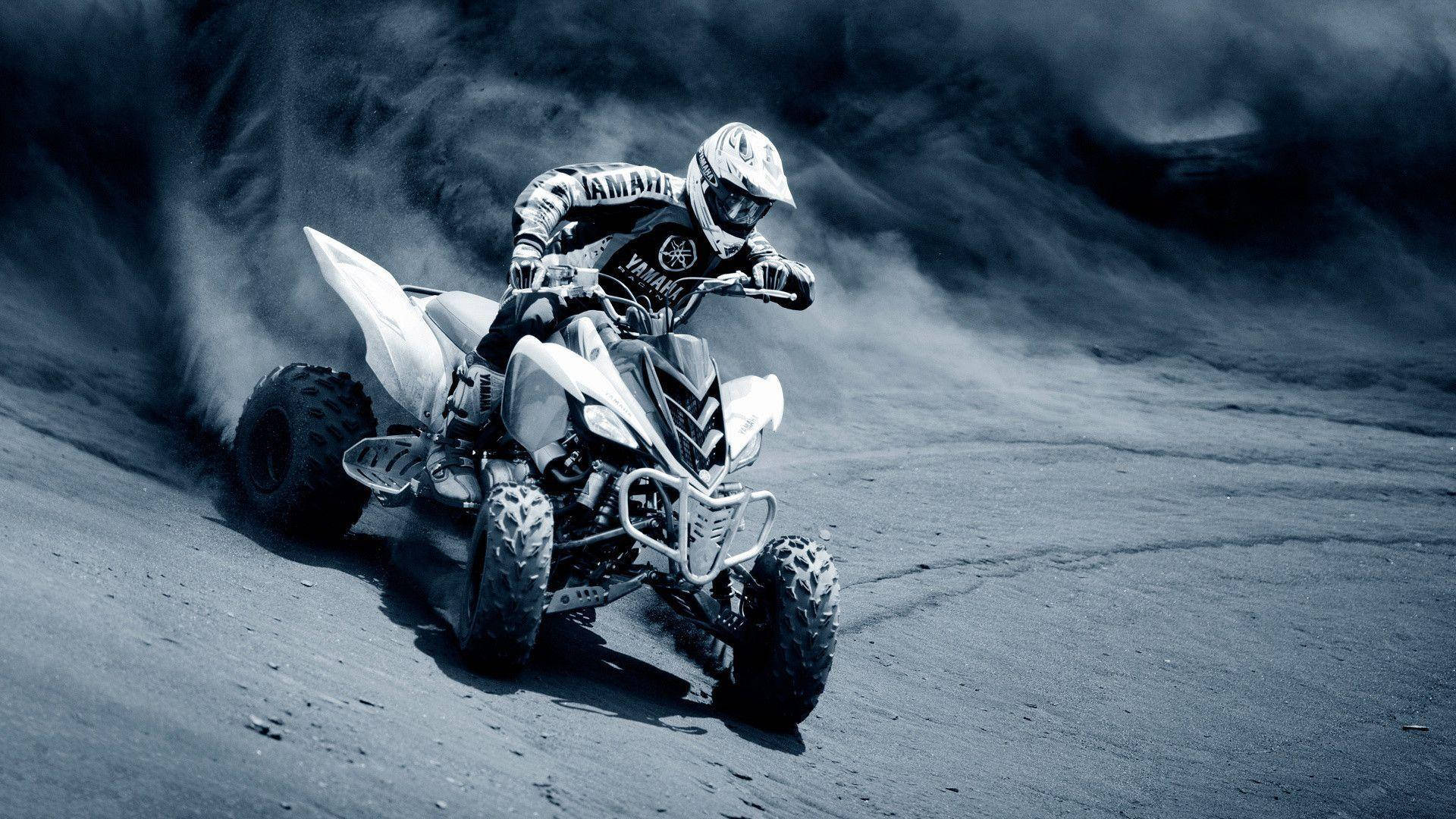 HD Sports 桌布 壁紙 — 一名騎士在白色Yamaha ATV上傾斜入彎，在崎嶇的泥地賽道上揚起灰塵，在戲劇性的藍色調燈光下。