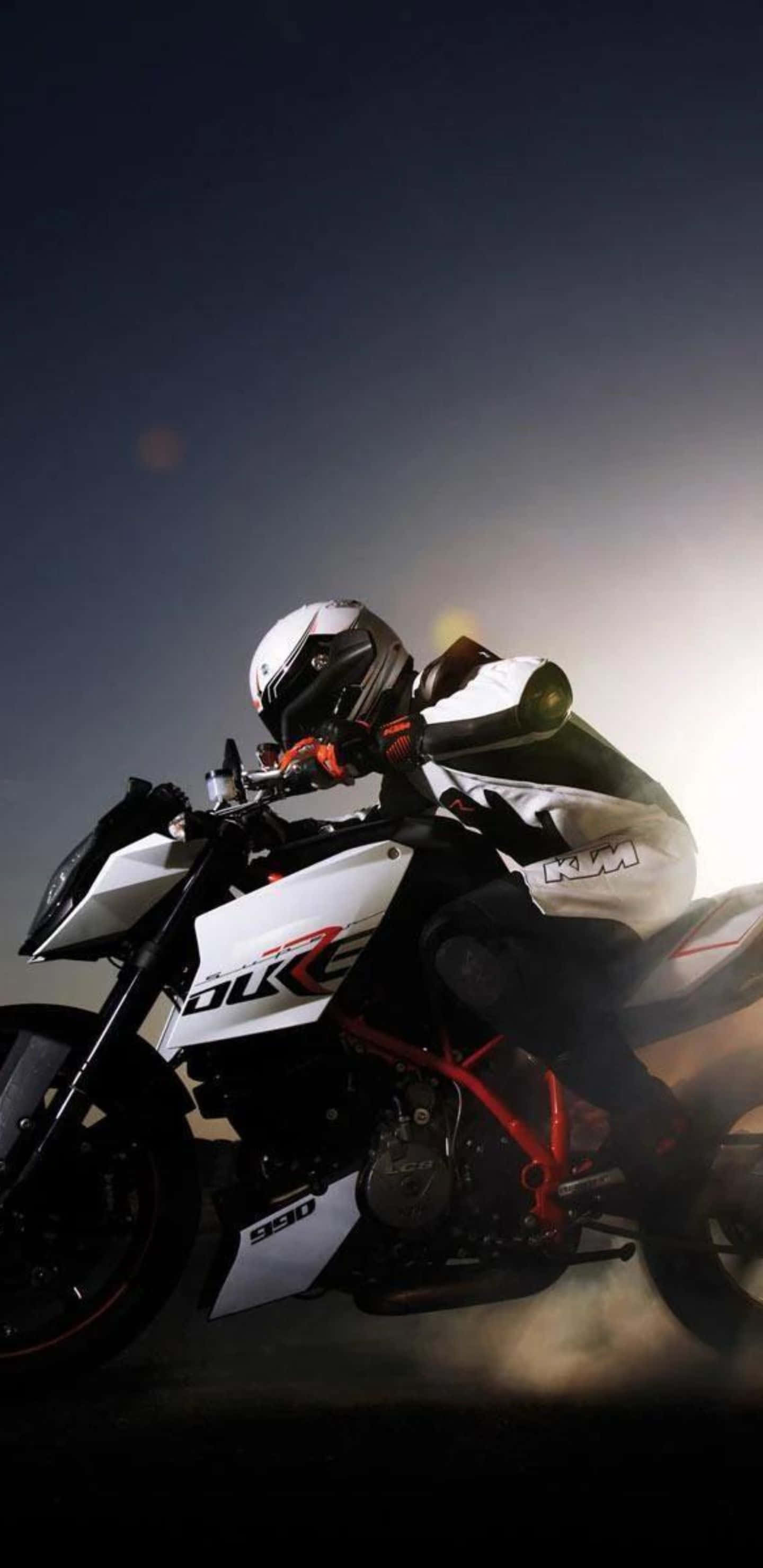 Pixel 3xl Bikes 桌布 壁紙 — 一名騎士在白色和紅色的KTM Duke 990摩托車上傾斜入彎，背景是黑暗的天空，帶有戲劇性的背光效果。