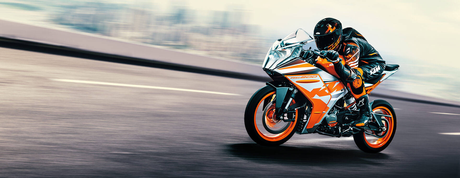 KTM RC 200 桌布 壁紙 — 一名騎士在鮮豔的橙色和白色KTM運動機車上傾斜入彎，在模糊的高速公路上飛馳。