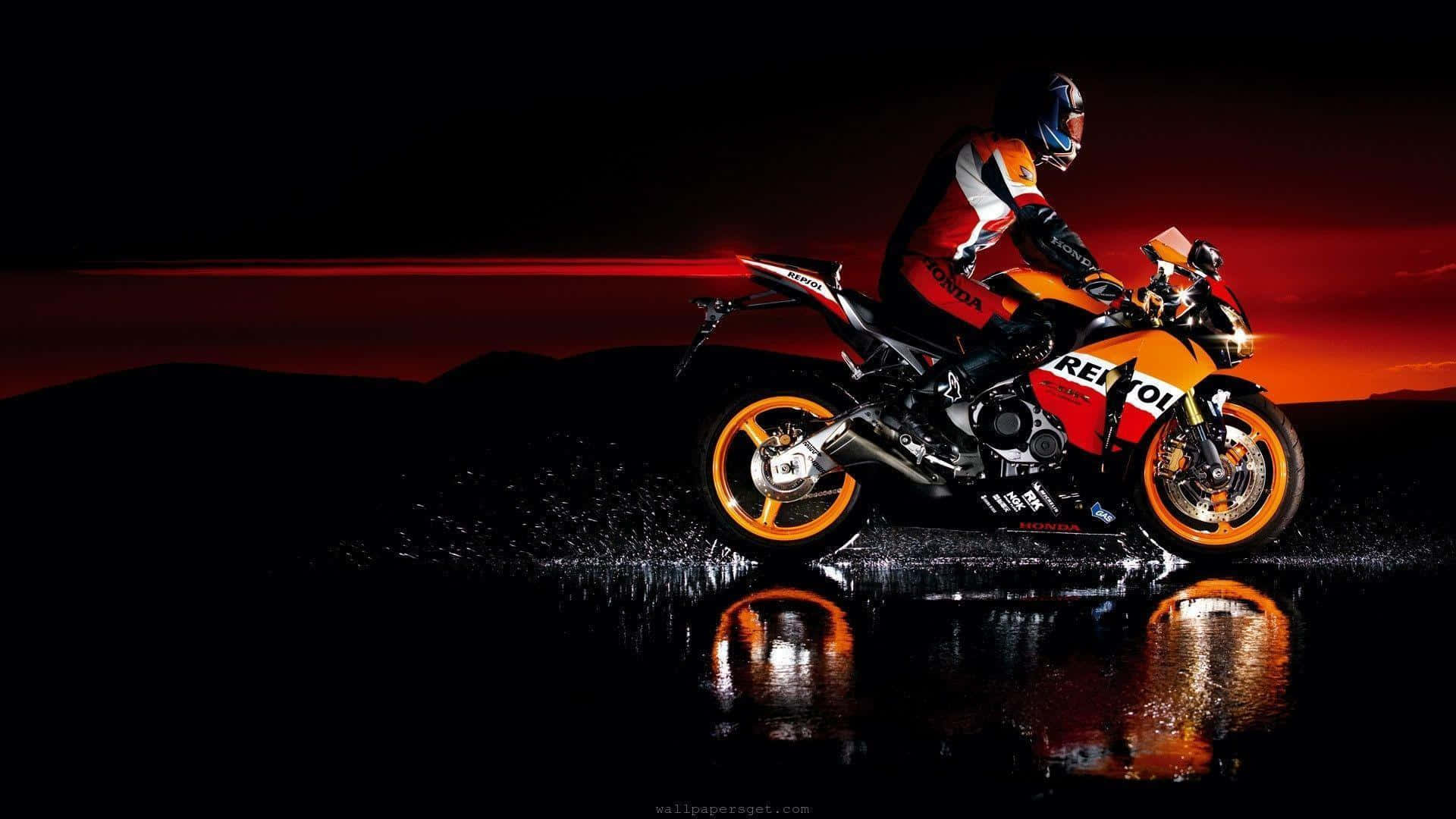  壁紙 — 一名騎士騎著紅橙色的Repsol Honda摩托車，在日落時分的潮濕反光表面上飛馳，背景是火紅的天空和黑色剪影山脈。