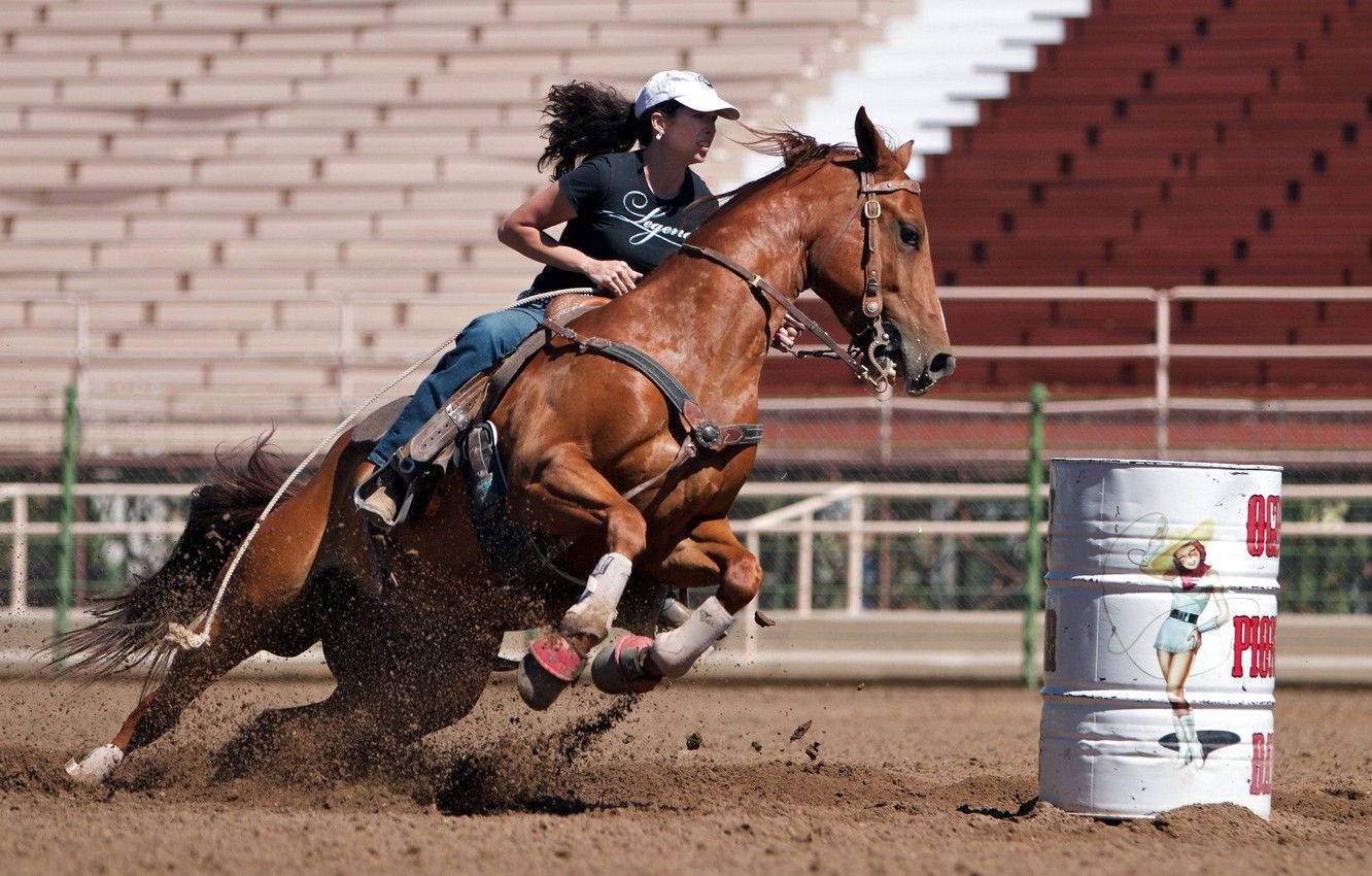 Barrel Racing 桌布 壁紙 — 一名騎手在奔騰的栗色馬上傾身轉過一個急彎，在牛仔競技場中揚起泥土圍繞一個白色桶子。