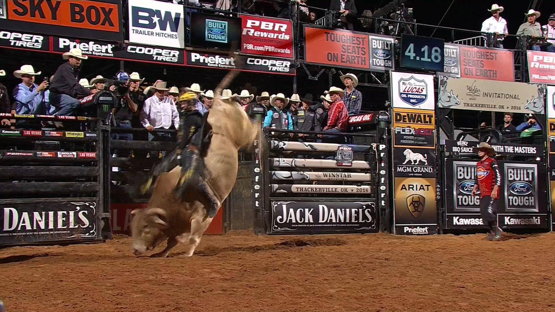 Bull Riding 桌布 壁紙 — 一名騎牛士在明亮的體育場燈光下，於牛仔競技場中緊抓著一頭狂跳的公牛，觀眾和贊助商橫幅環繞著泥土場地。