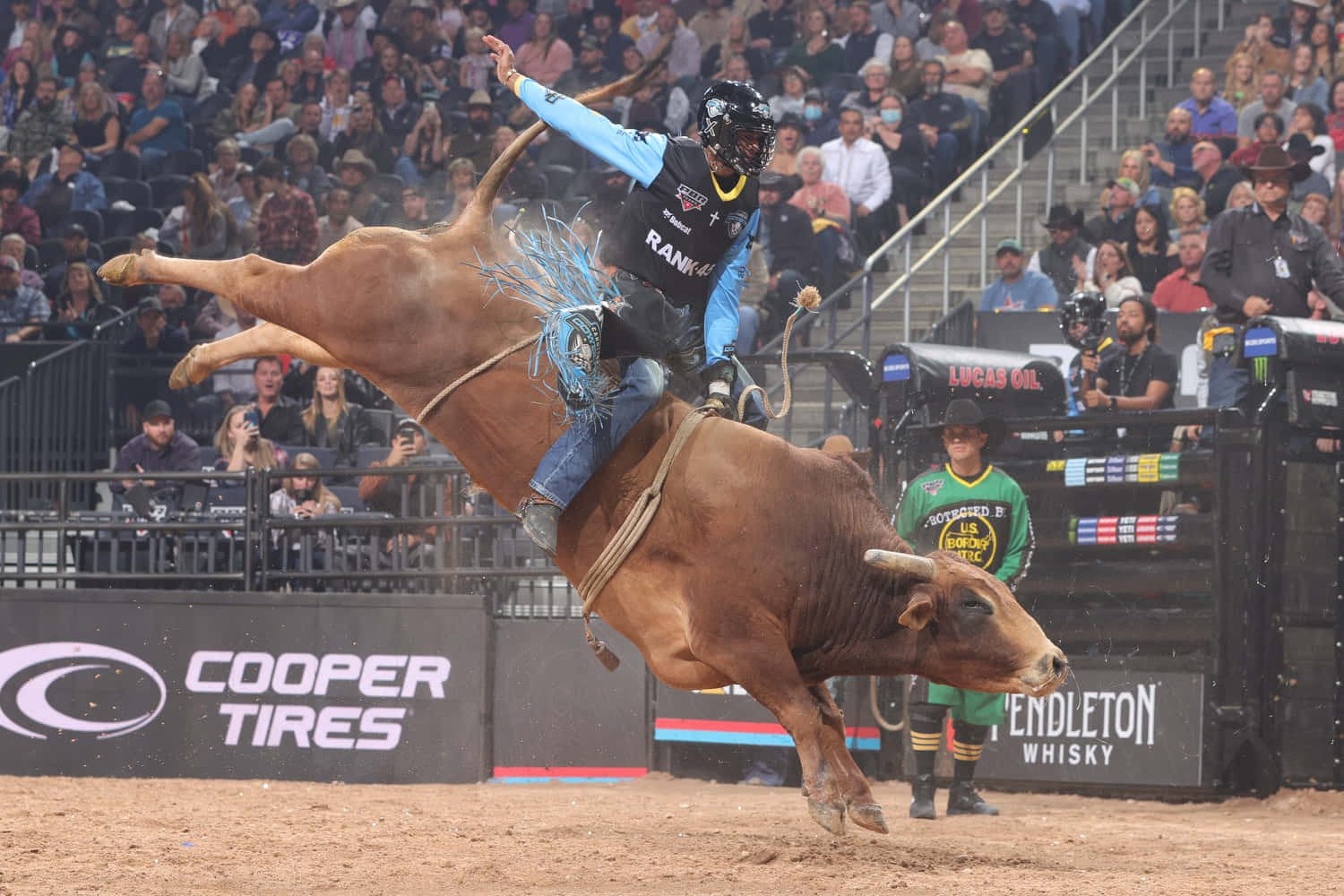 Bull Riding 桌布 壁紙 — 一名騎牛士在牛仔競技場中緊抓著一頭騰躍的棕色公牛，觀眾從看台觀看。
