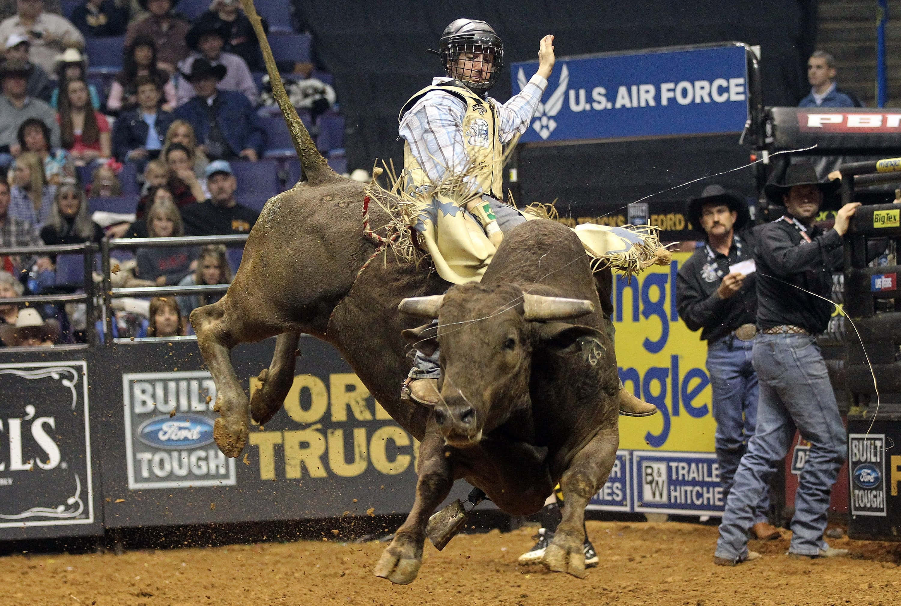 Bull Rider 桌布 壁紙 — 一名騎牛士在牛仔競技場緊緊抓住一隻猛跳的公牛，觀眾在看台觀看。