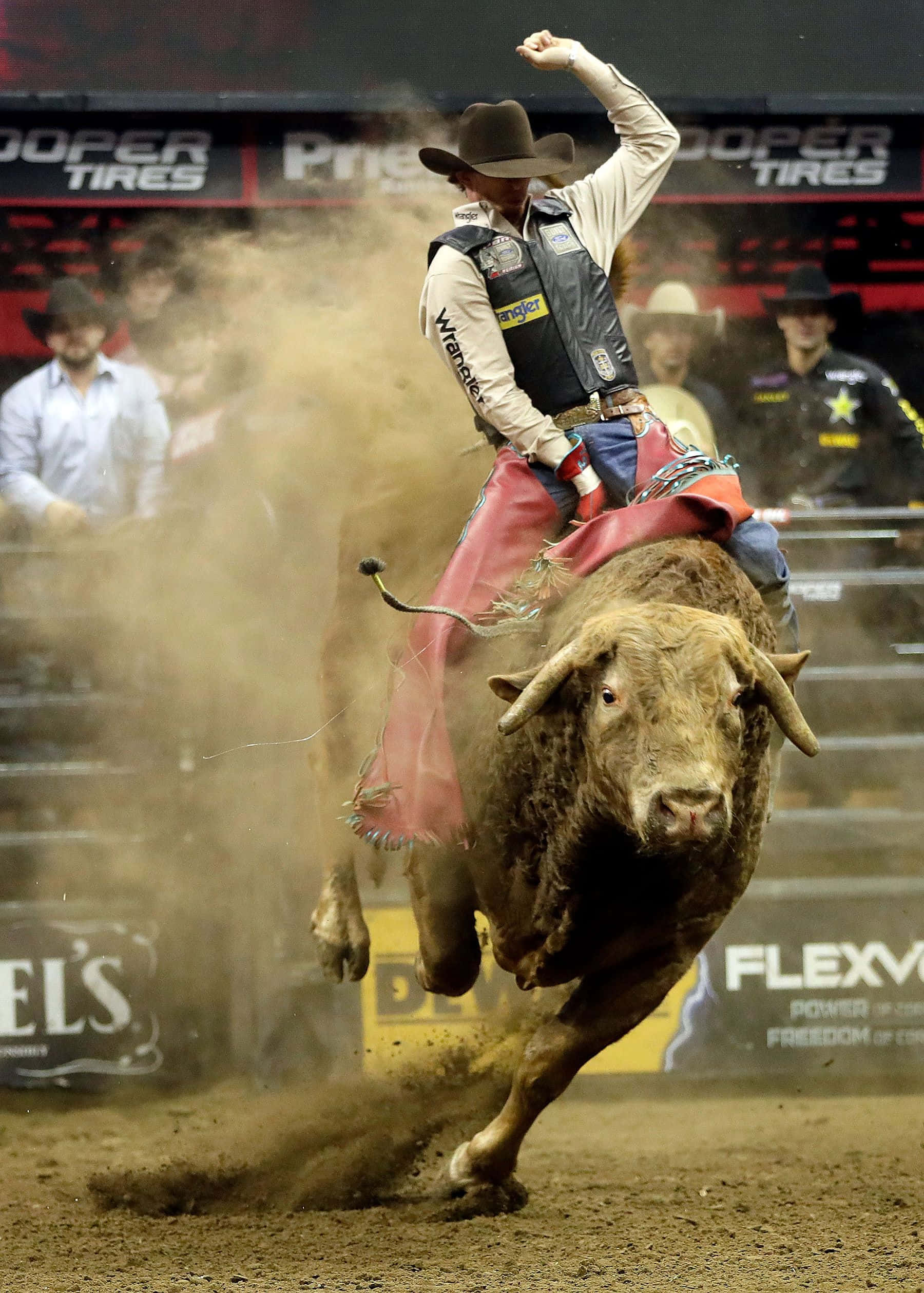 Bull Rider 桌布 壁紙 — 一名騎牛士緊抓著一頭狂跳的公牛，周圍塵土飛揚，在明亮的燈光下的牛仔競技場中。
