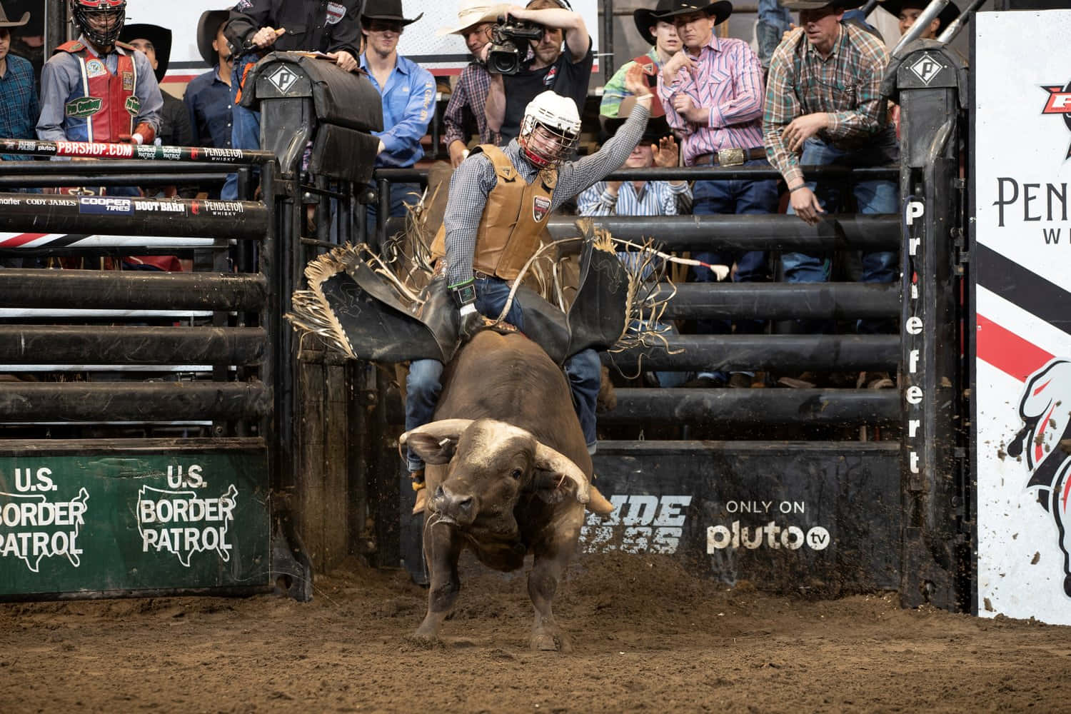 Bull Riding 桌布 壁紙 — 一名騎牛士緊抓著在牛仔競技場中猛烈甩動的公牛，觀眾在欄杆後觀看。