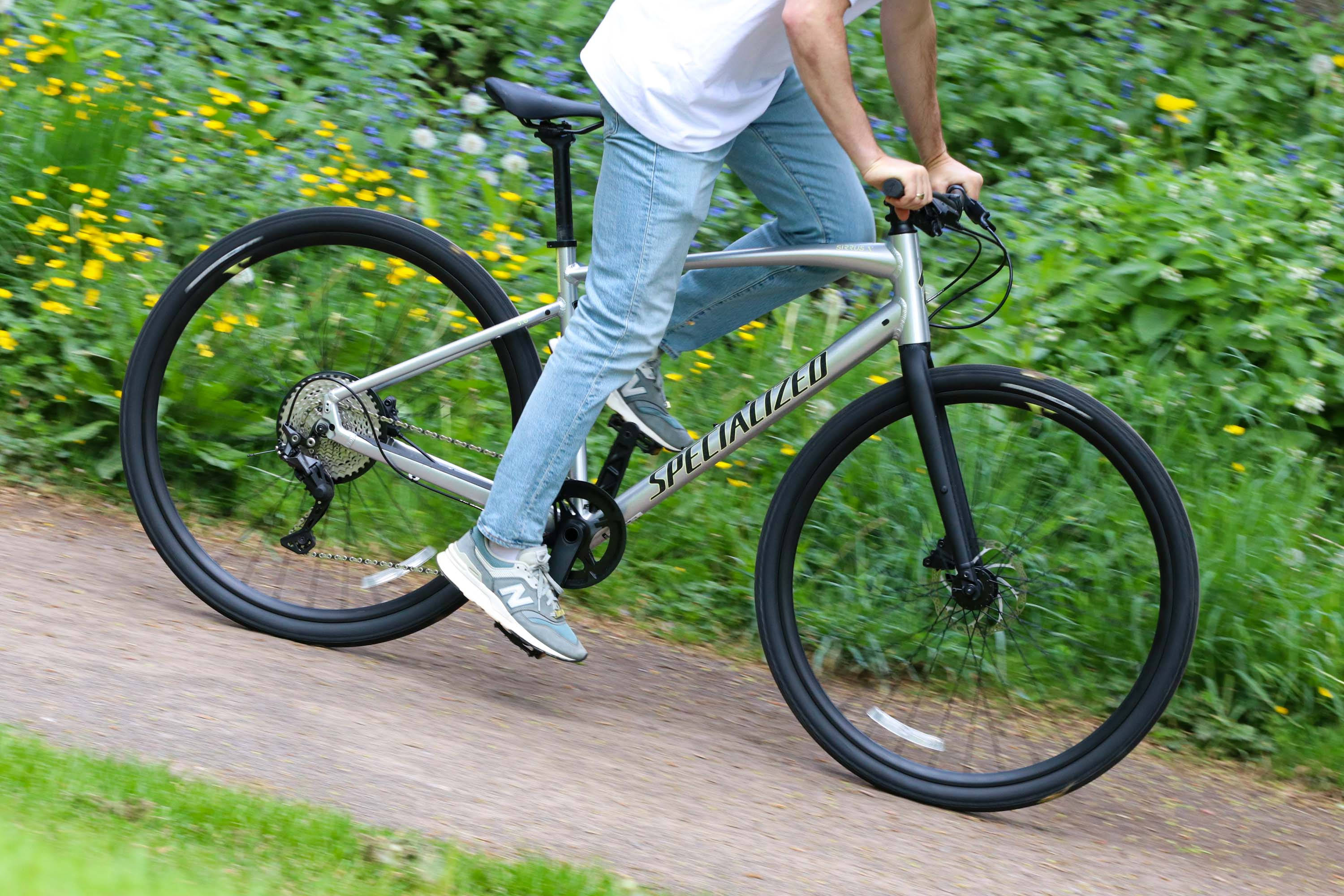 腳踏車 桌布 壁紙 — 一名騎自行車的人踩著銀色Specialized登山車，沿著碎石路穿過色彩繽紛的野花和綠色樹葉。